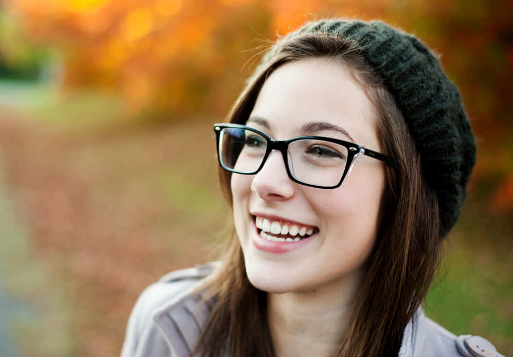 Smile 桌布 壁紙 — 一位戴眼鏡和針織帽的年輕女子在充滿活力的秋日背景下開懷大笑。