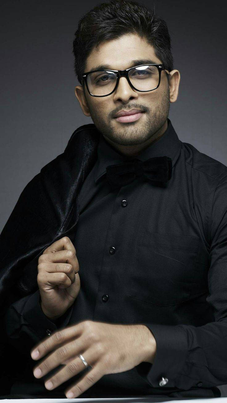 Allu Arjun 桌布 壁紙 — 一位戴眼鏡和領結的時尚男士，在深色工作室背景下自信地穿著黑色西裝擺姿勢。