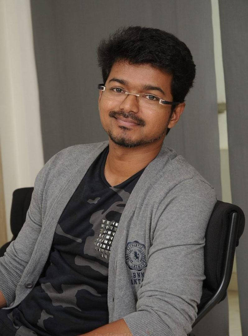 vijay HD 桌布 壁紙 — 一位戴眼鏡和鬍子的年輕男子放鬆地坐在椅子上，穿著灰色開襟衫，內搭迷彩T恤。