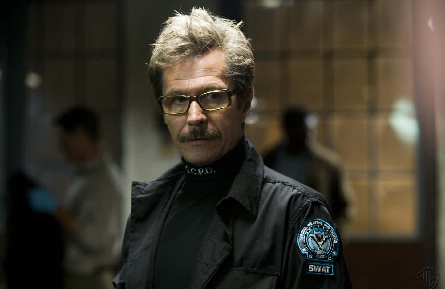 Commissioner Gordon 桌布 壁紙 — 一位戴眼鏡和鬍子的灰髮警察在昏暗的走廊裡凝視著。