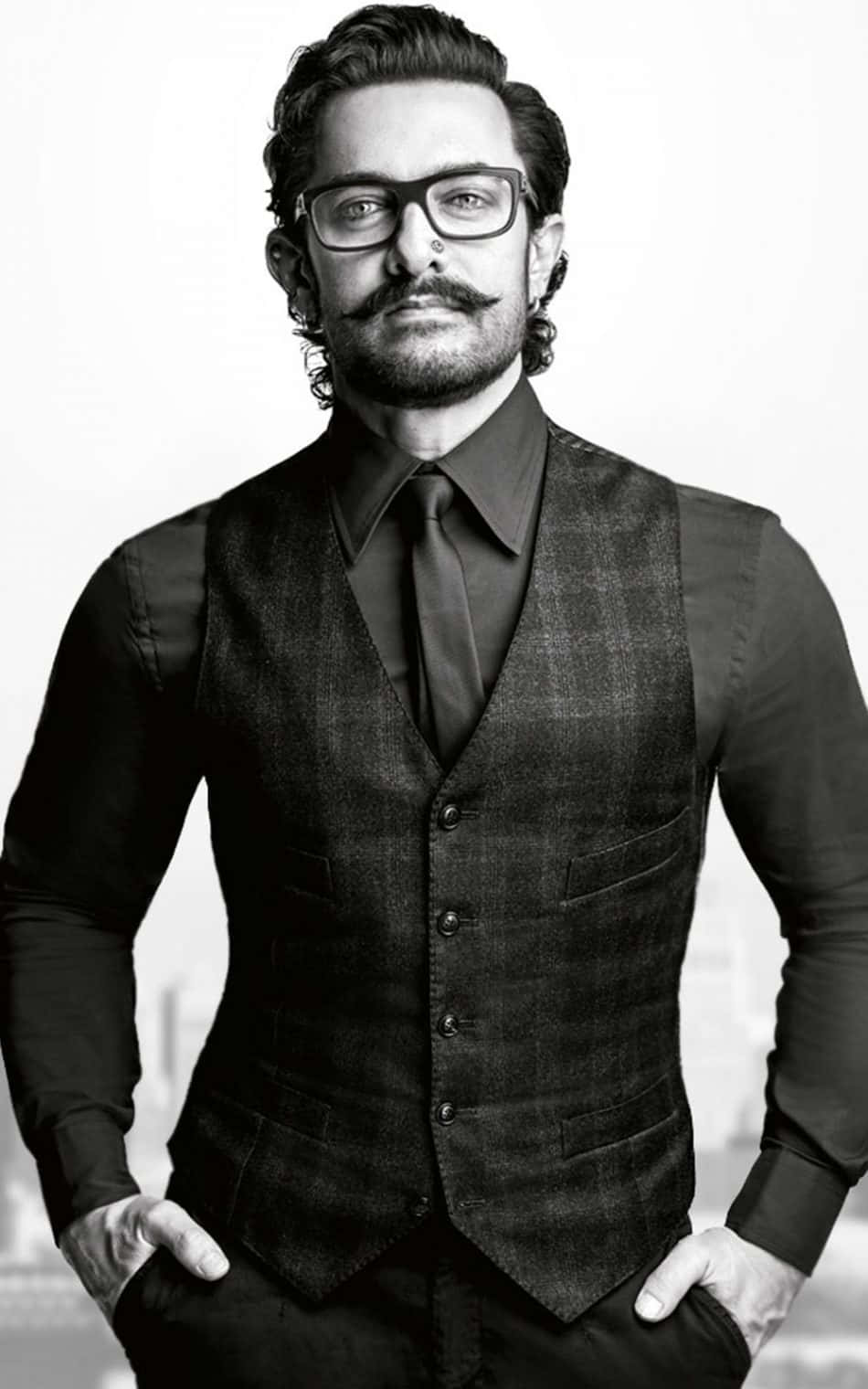 Aamir Khan 桌布 壁紙 — 一位戴眼鏡和鬍子的男士，穿著黑色背心和襯衫，自信地站在純色背景前。