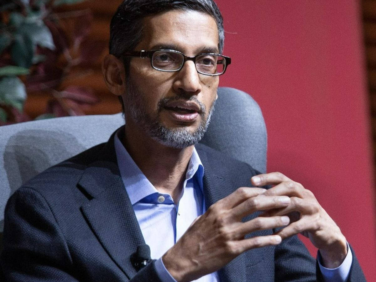 google 桌布 壁紙 — 一位戴眼鏡和鬍鬚的男人坐在灰色椅子上，對著紅牆說話。