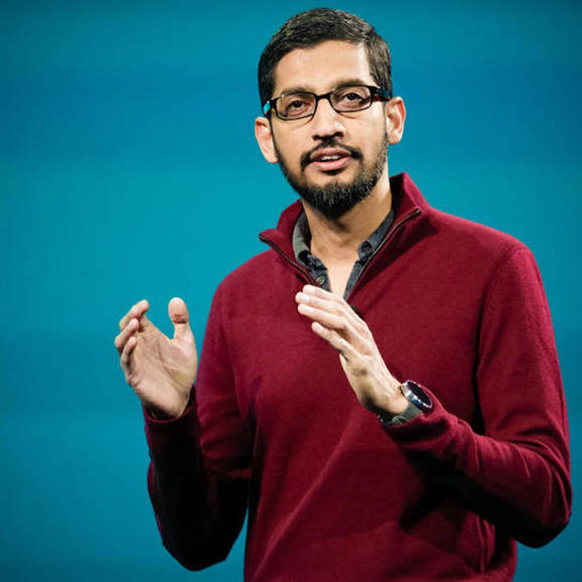 google 桌布 壁紙 — 一位戴眼鏡和鬍鬚的男子在純藍色背景前說話時做手勢。