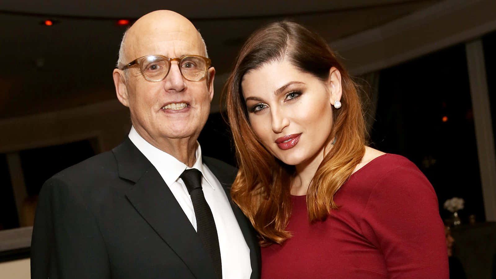 jeffrey tambor 桌布 壁紙 — 一位戴眼鏡的光頭男士和一位紅髮女士在溫暖燈光下的室內活動中一起擺姿勢。