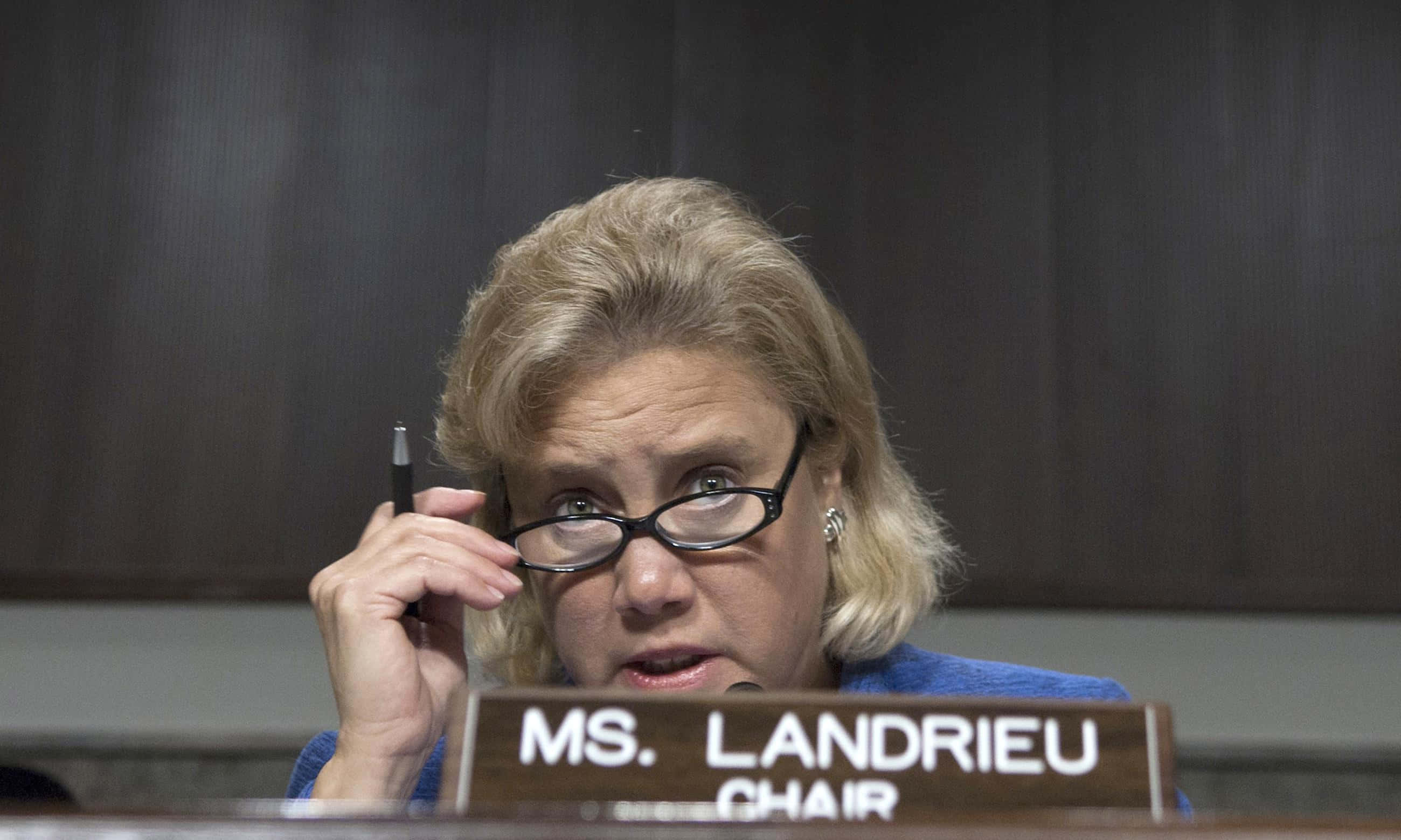 政治 桌布 壁紙 — 一位戴眼鏡的專注女性在寫有 'MS. LANDRIEU CHAIR' 的正式會議桌旁調整眼鏡。