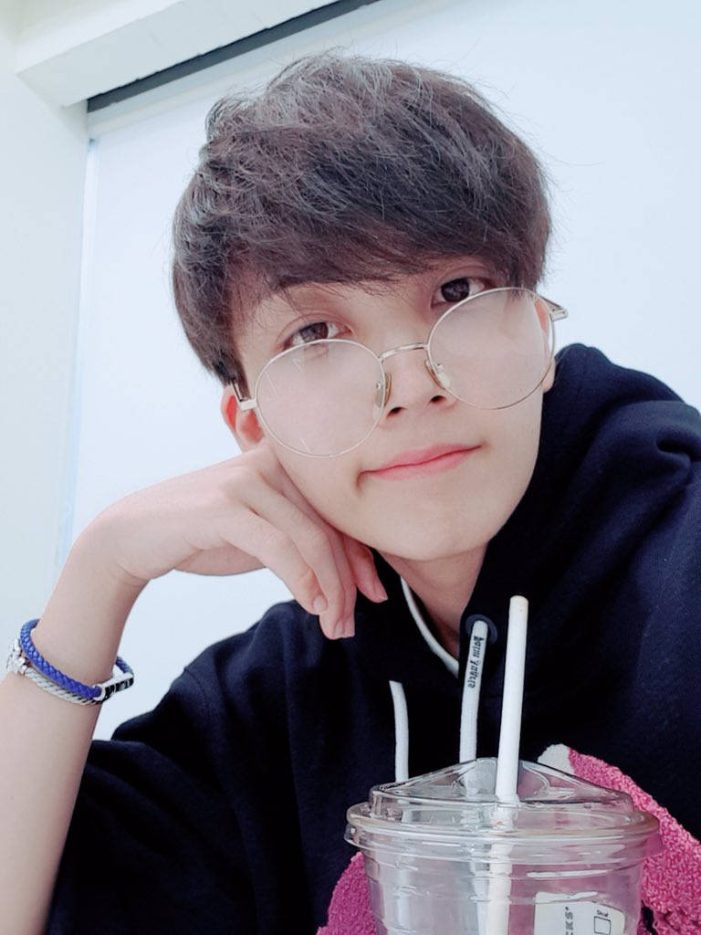 yoon jeonghan 桌布 壁紙 — 一位戴眼鏡的年輕人，在明亮的室內環境中，將下巴擱在手邊，旁邊放著一杯飲料。