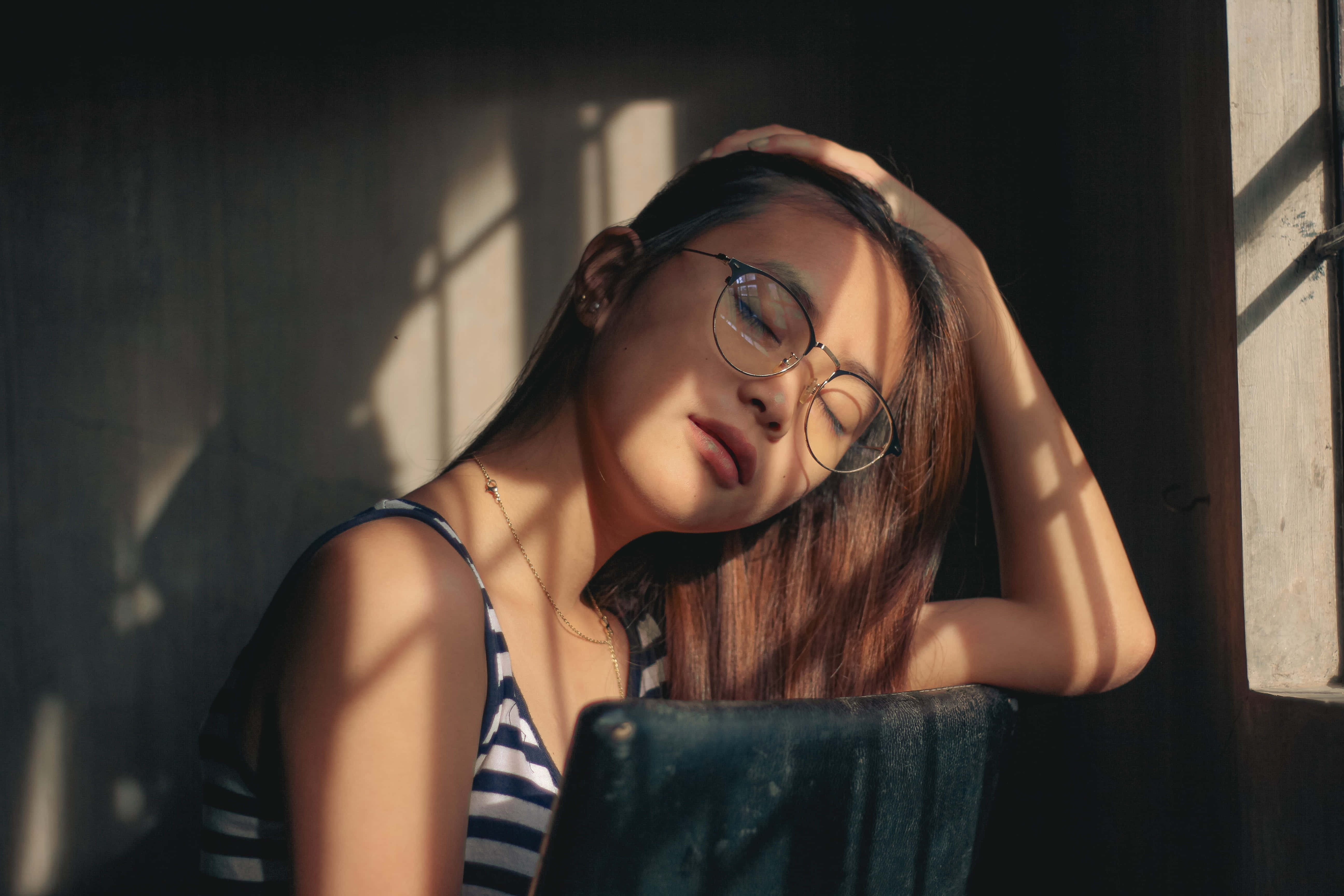 Teen Girl 桌布 壁紙 — 一位戴眼鏡的年輕女子將頭靠在窗框上，金色的陽光灑在她的臉龐和肩膀上。