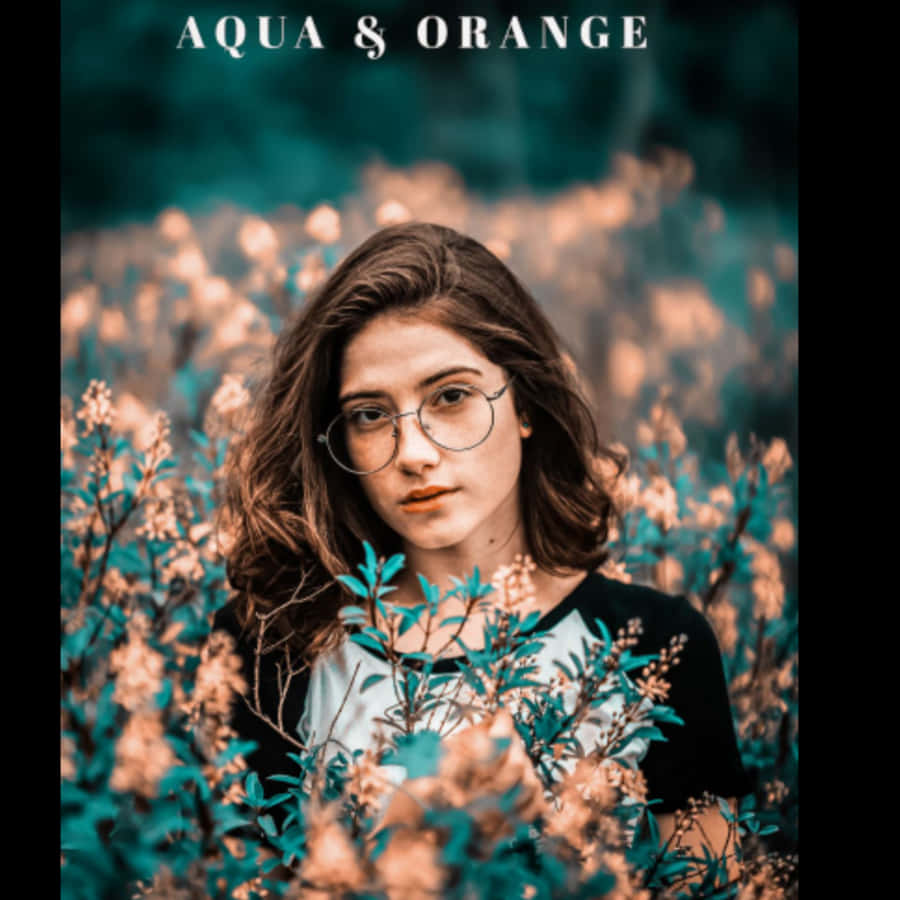 Lightroom Preset 桌布 壁紙 — 一位戴眼鏡的年輕女性站在柔和模糊的田野中，周圍是充滿活力的水藍色和橙色花朵。