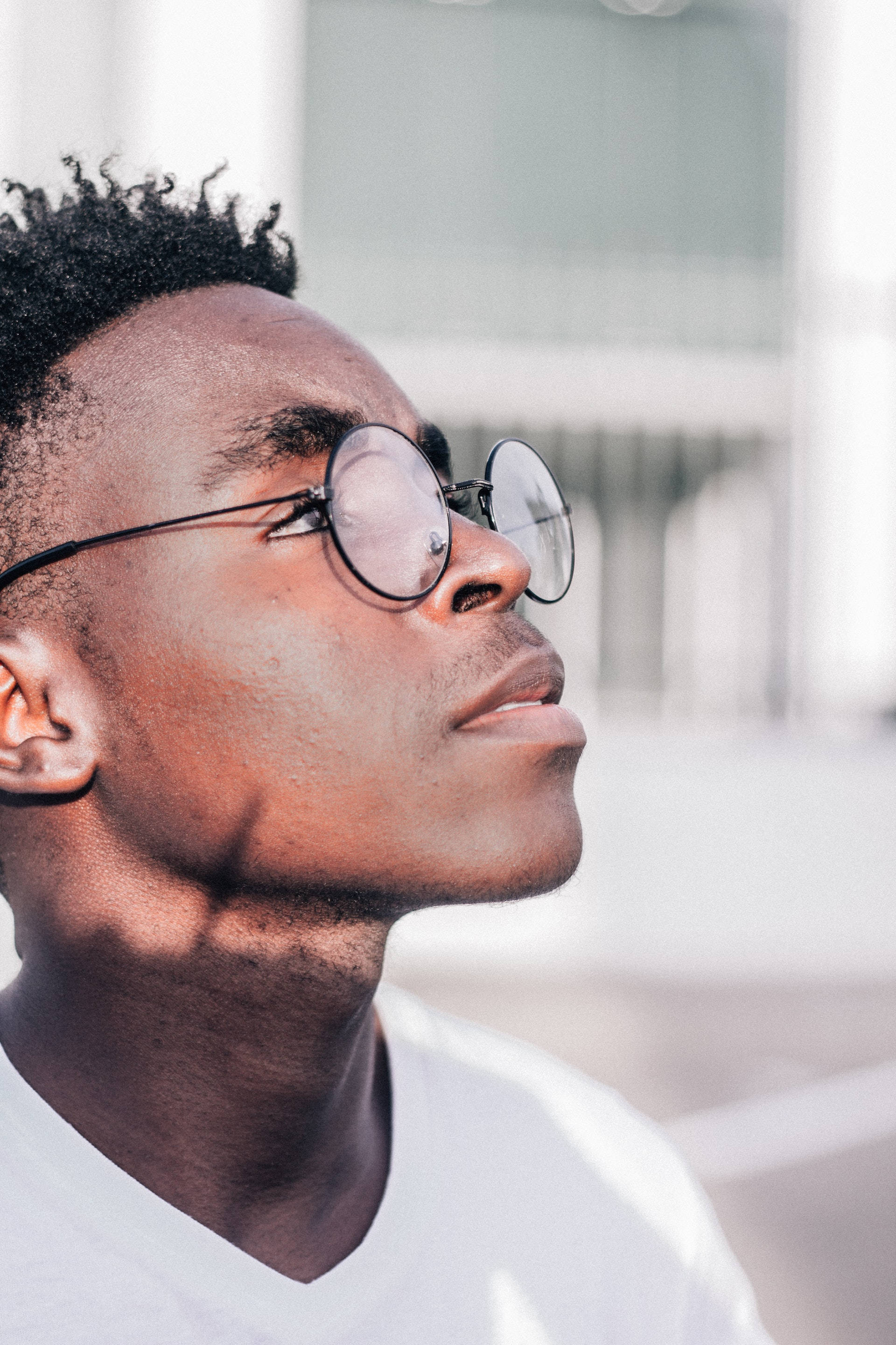 glasses 桌布 壁紙 — 一位戴眼鏡的年輕男子在陽光普照的城市環境中向上凝視，背景柔和模糊。
