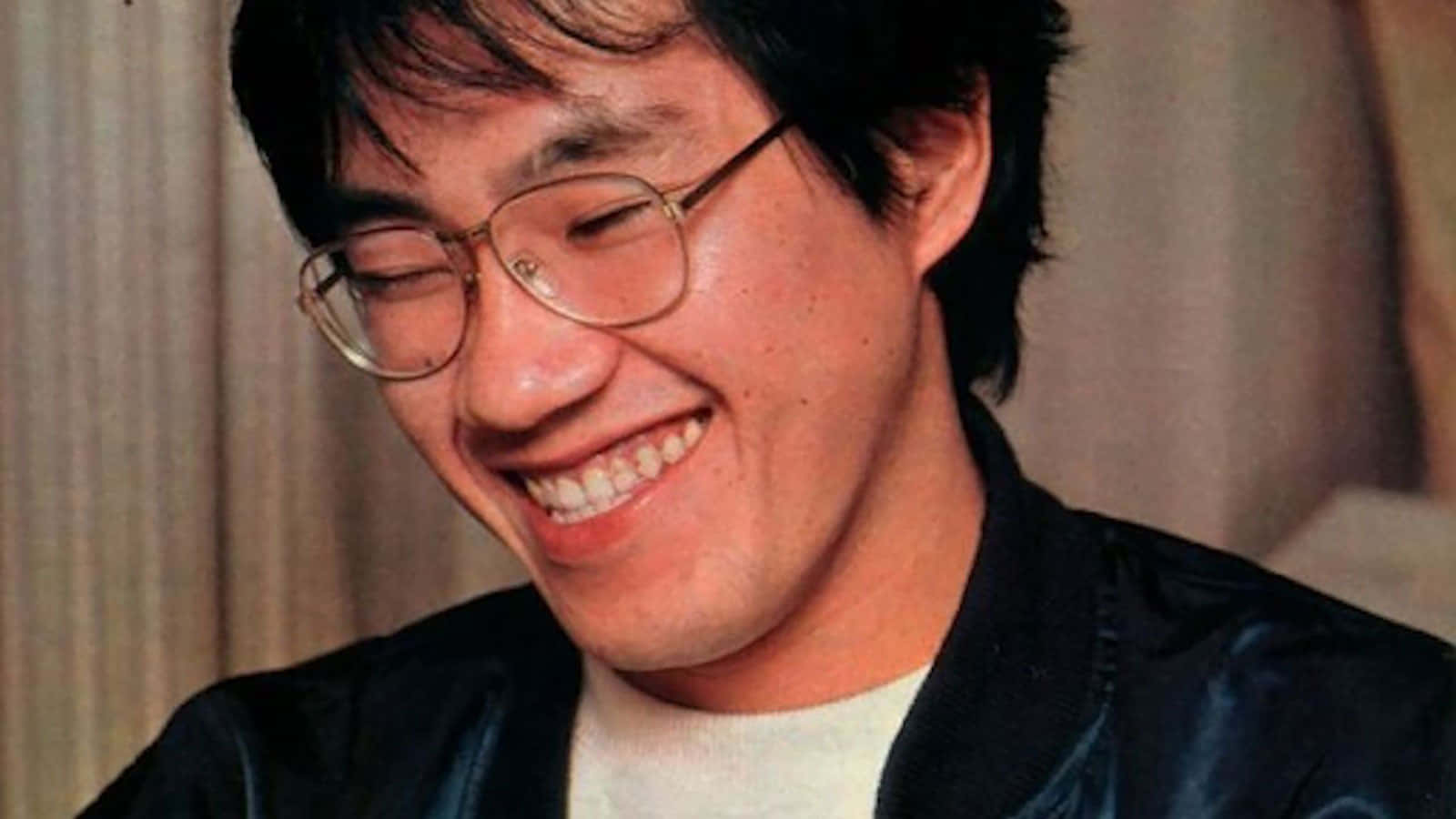 Akira Toriyama 桌布 壁紙 — 一位戴眼鏡的快樂男士，身穿黑色外套內搭白襯衫，露出溫暖的笑容。