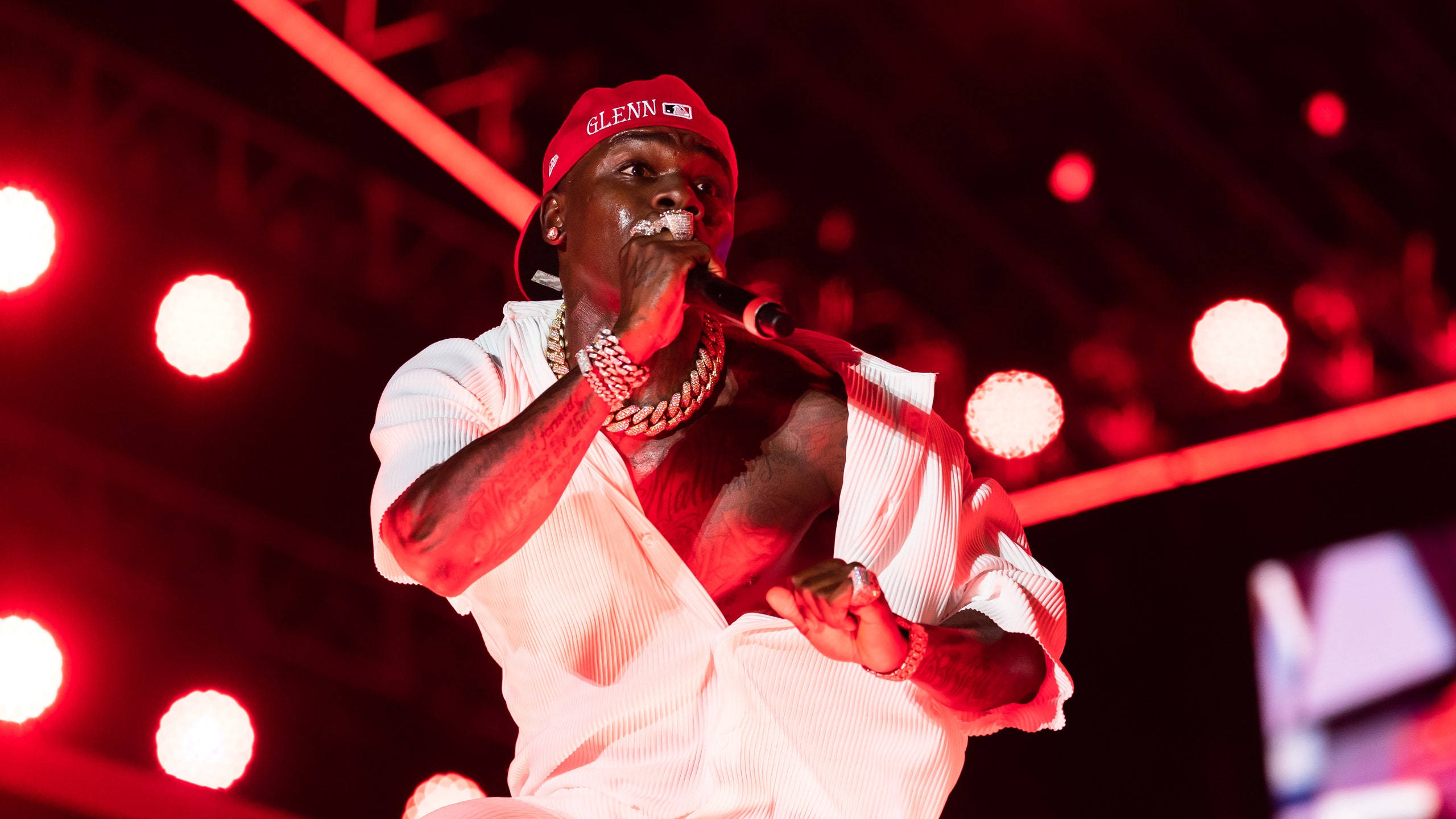Dababy 桌布 壁紙 — 一位戴紅帽、穿白襯衫的饒舌歌手在強烈的紅色舞台燈光下，煙霧繚繞，熱情表演。