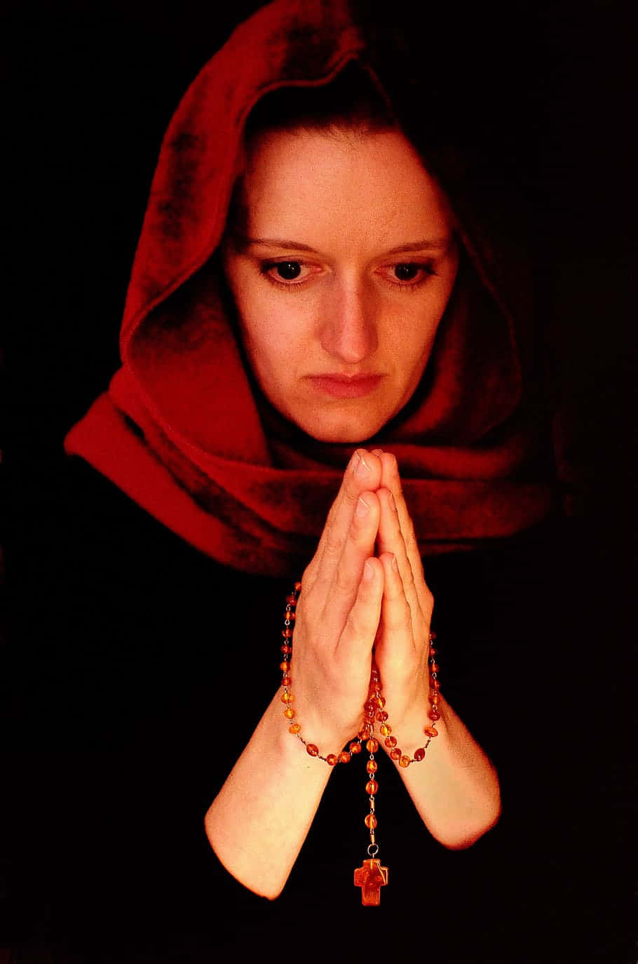 Praying 桌布 壁紙 — 一位戴紅帽的女人在黑暗背景中，柔和燈光下，手持玫瑰經祈禱。
