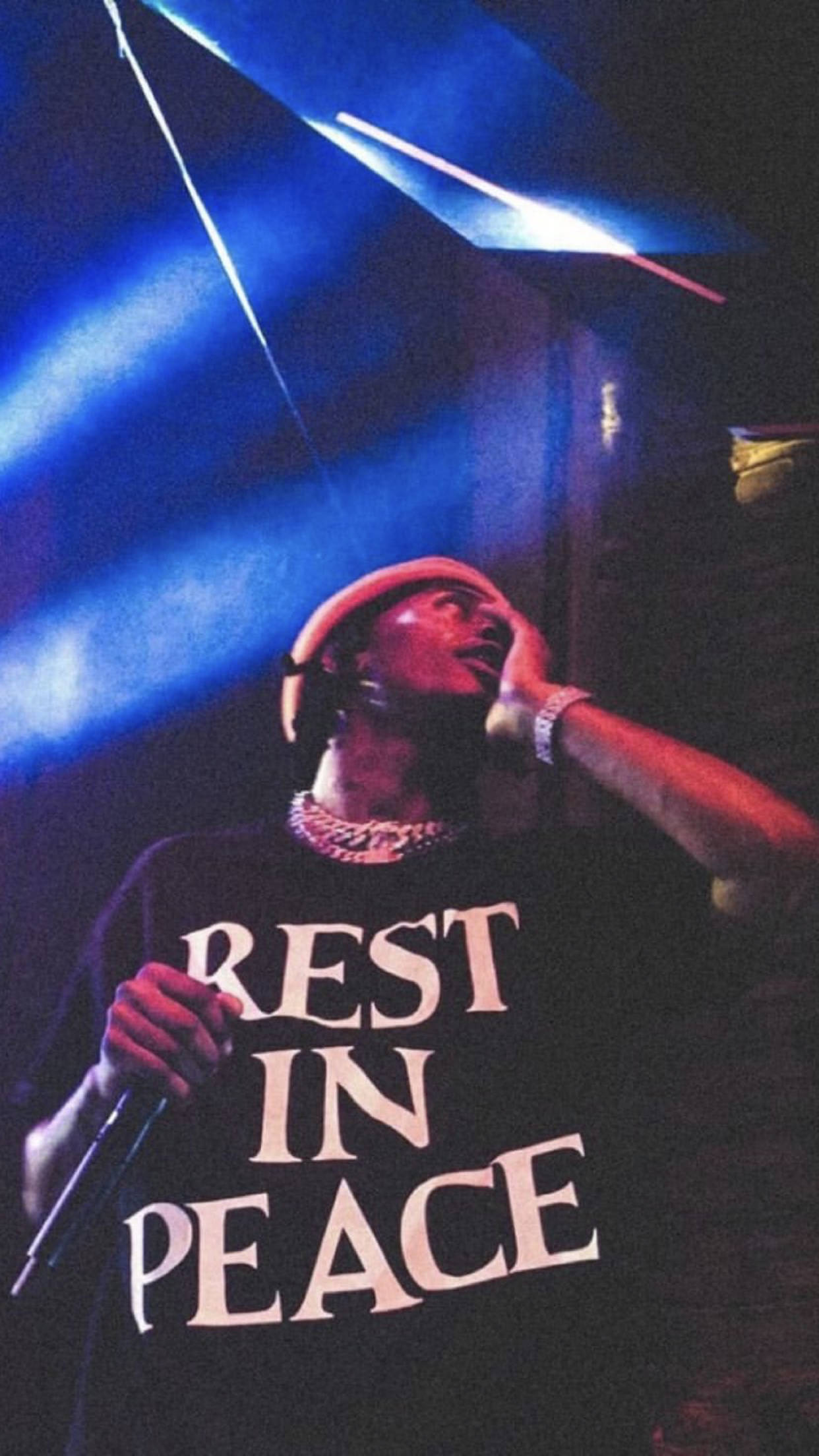 Rappers 桌布 壁紙 — 一位戴紅色帽、身穿「REST IN PEACE」T恤的表演者在戲劇性的藍色舞台燈光下唱歌。