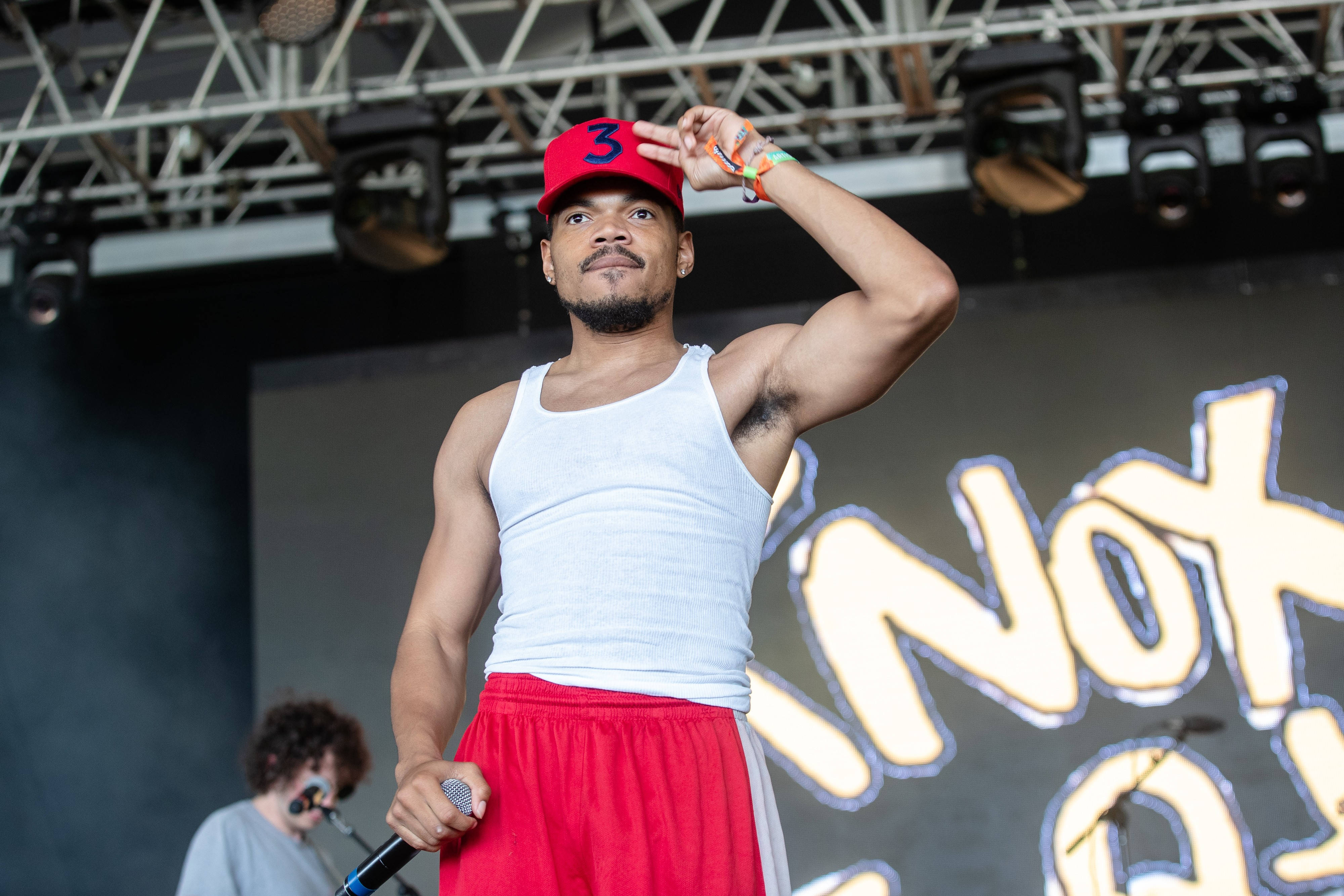 chance 桌布 壁紙 — 一位戴紅色帽子、身穿白色背心的男性表演者在舞台上，在明亮燈光及發光背景下手持麥克風。