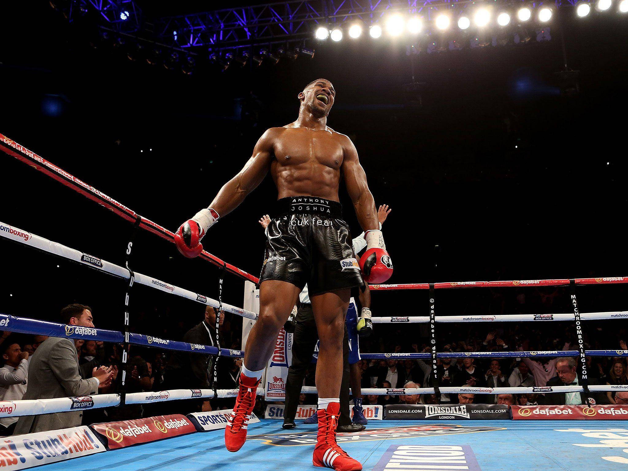 Anthony Joshua 桌布 壁紙 — 一位戴紅色手套、穿黑色短褲的勝利拳擊手，在燈光明亮的擂台上與歡呼的粉絲一起慶祝勝利。