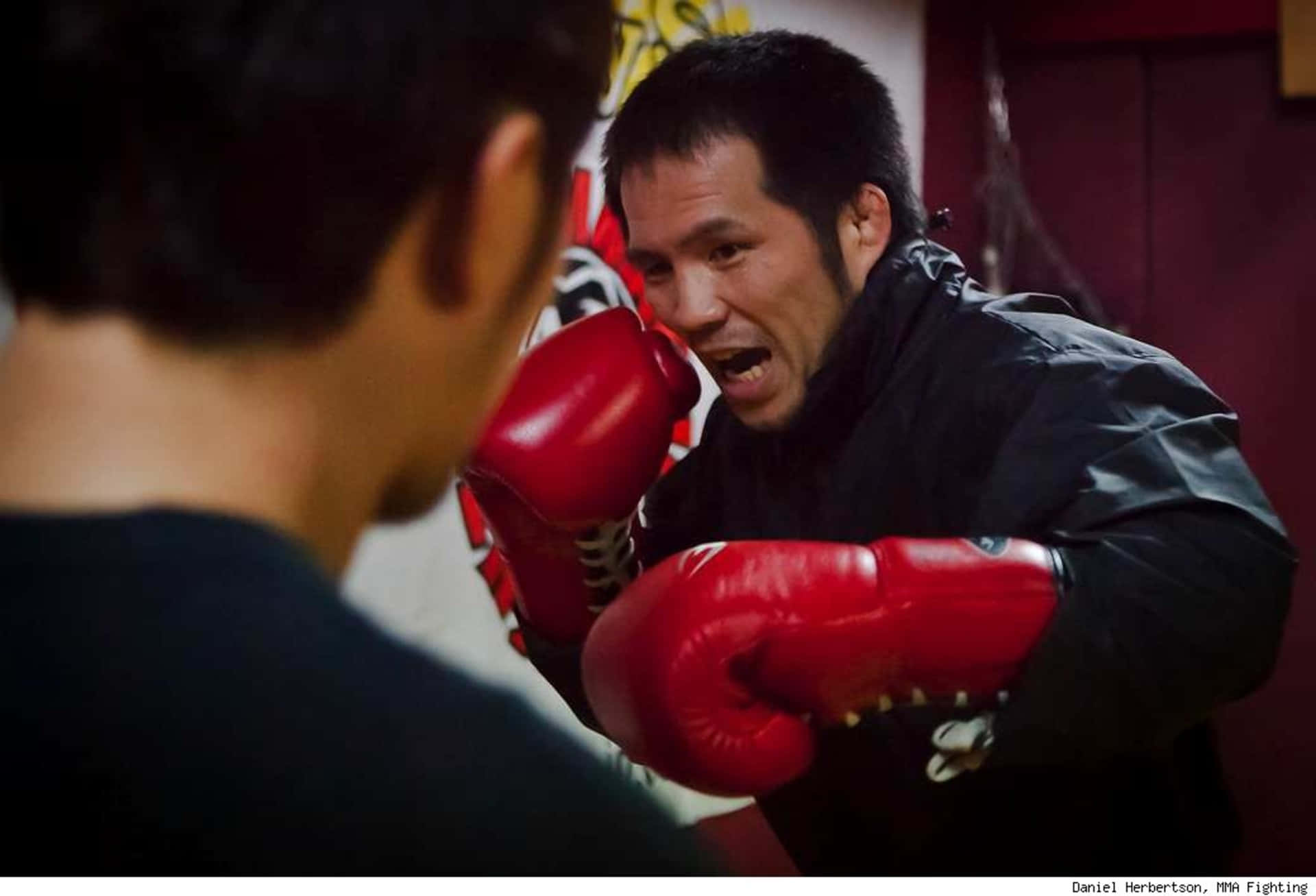 MMA 桌布 壁紙 — 一位戴紅色手套的拳擊手在昏暗的健身房訓練時激烈咆哮。