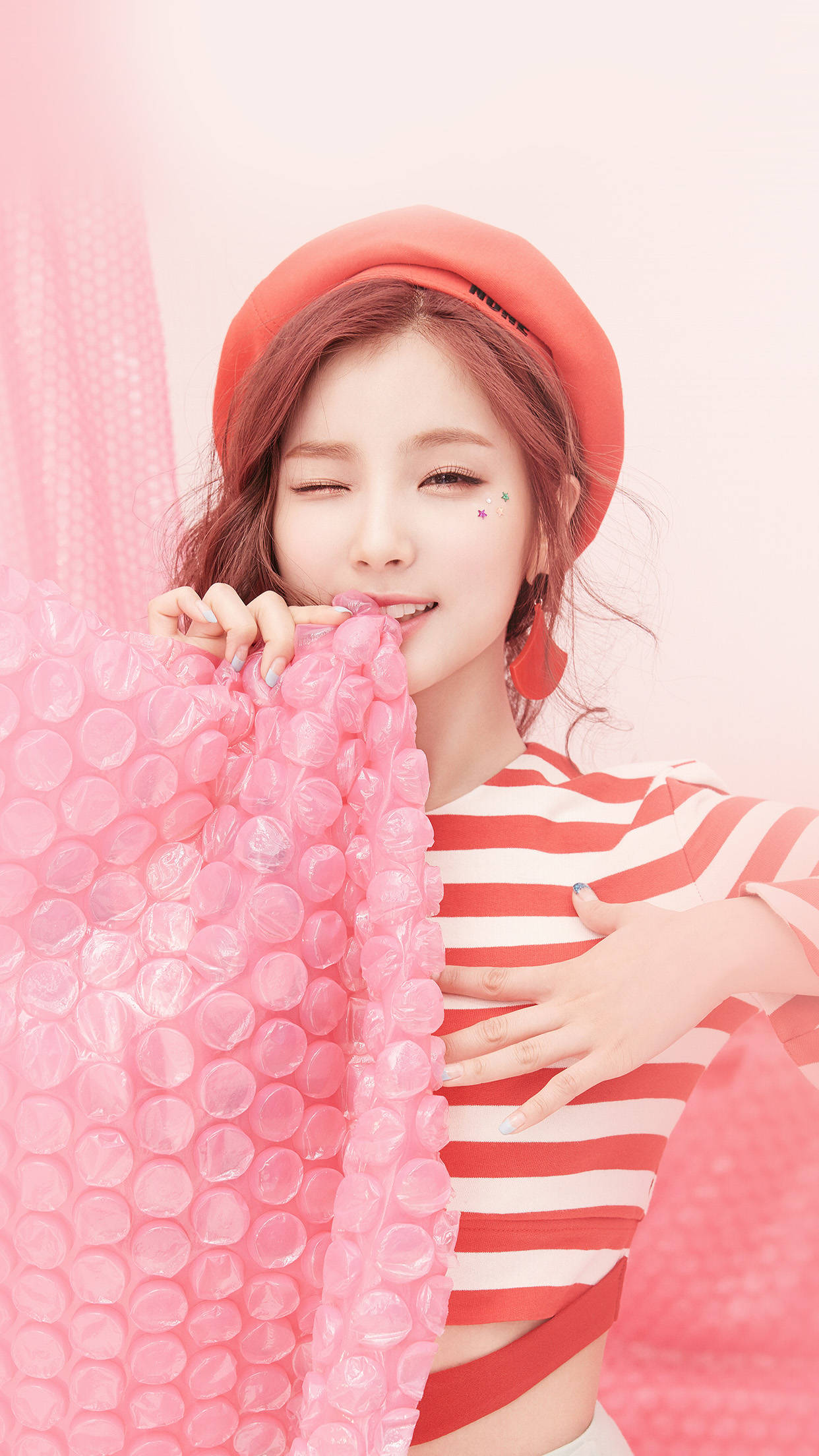 Cute Pink Girl 桌布 壁紙 — 一位戴紅色貝雷帽、穿條紋上衣的年輕女子，在柔和的粉紅色背景前，俏皮地拿著粉紅色泡泡紙。