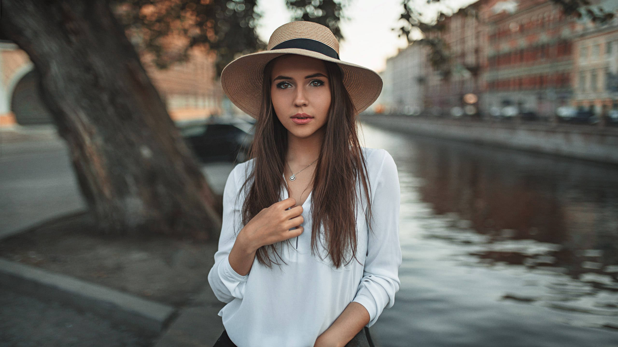 women 桌布 壁紙 — 一位戴草帽的年輕女子站在城市的運河旁，在柔和的金色光芒中平靜地凝視著相機。