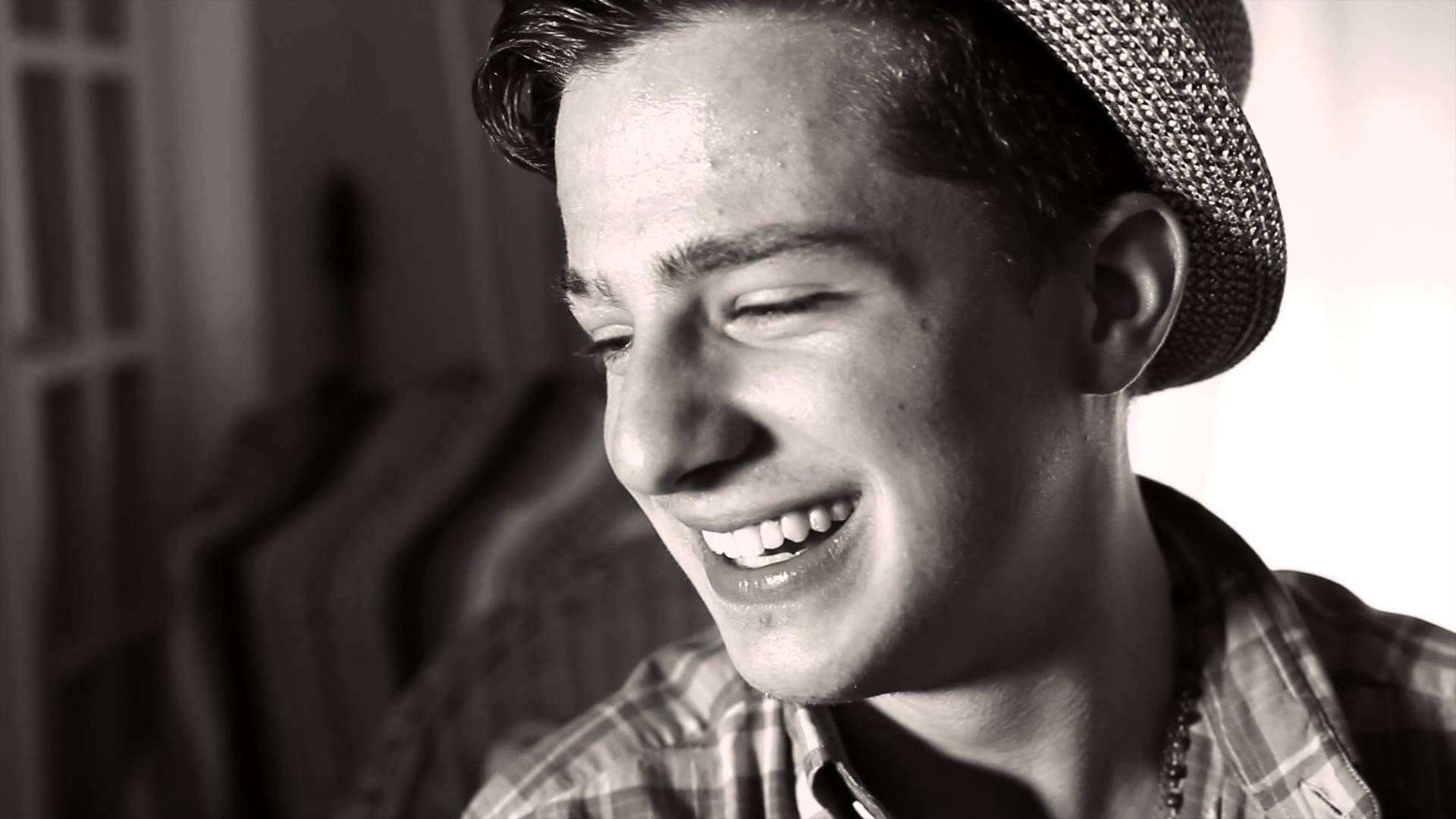 Charlie Puth 桌布 壁紙 — 一位戴草帽的年輕男子在柔和光線的室內環境中，以單色濾鏡開心大笑。