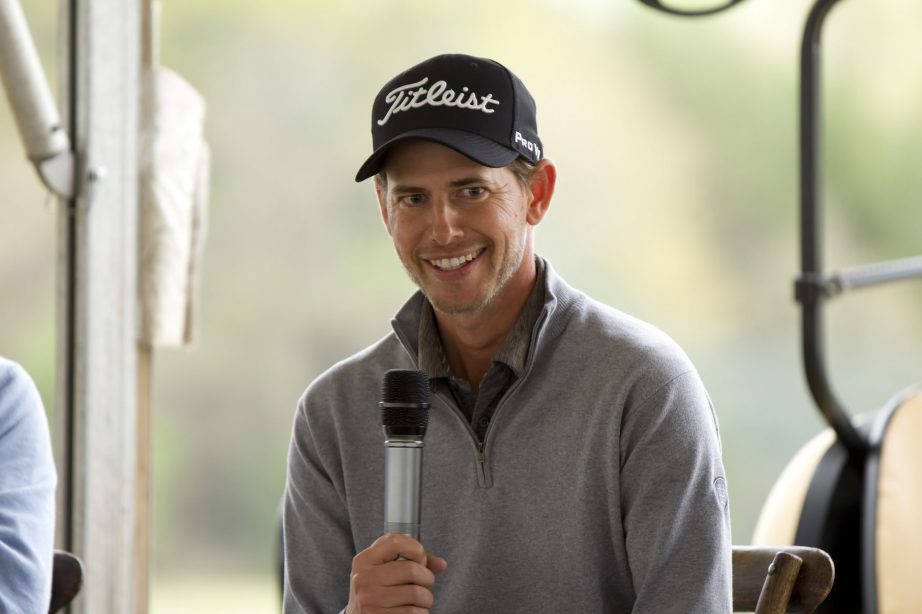 高爾夫 桌布 壁紙 — 一位戴著 Titleist 帽子的微笑高爾夫球手，在日間活動中坐在高爾夫球車上拿著麥克風。