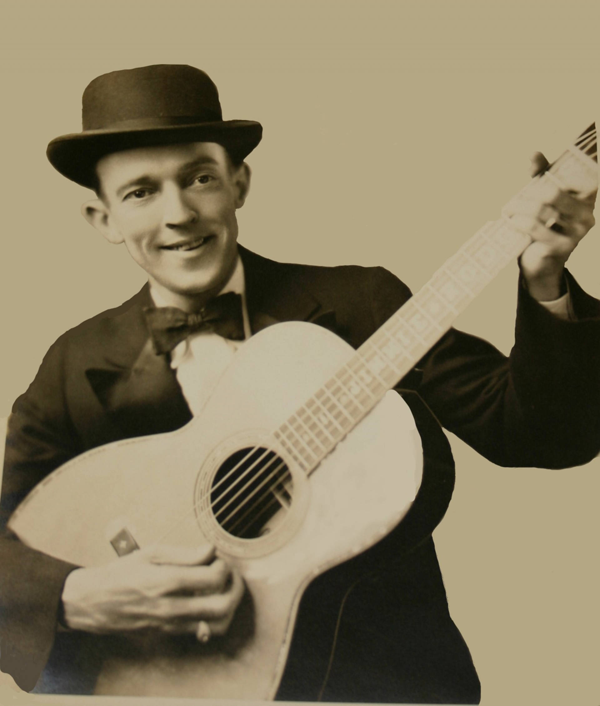guitar player 桌布 壁紙 — 一位戴著圓頂硬禮帽和領結的微笑男子，在純色復古背景前抱著一把原聲吉他。