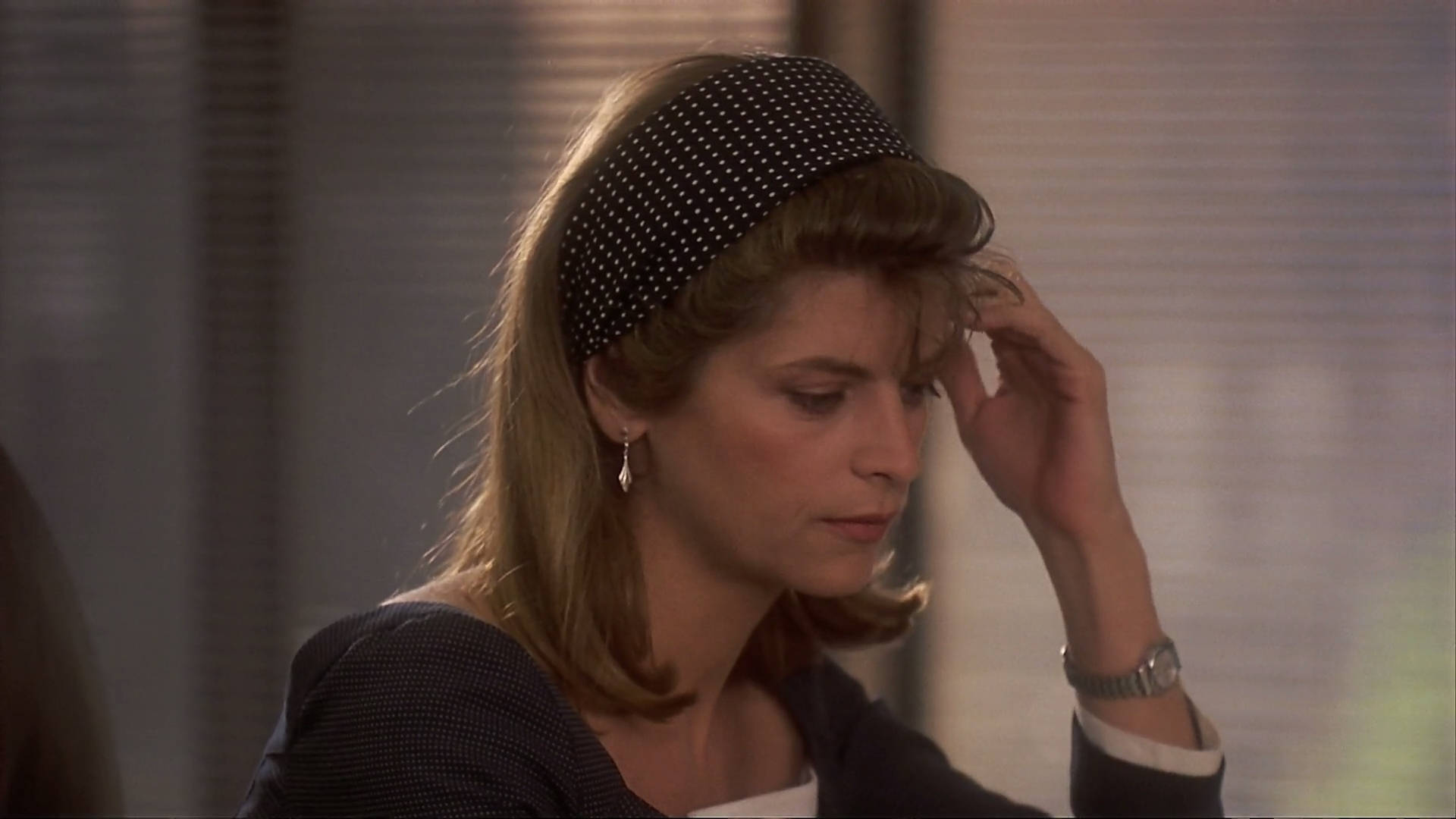 Kirstie Alley 桌布 壁紙 — 一位戴著圓點髮帶的女性在柔和光線的室內環境中低頭輕觸自己的頭髮。