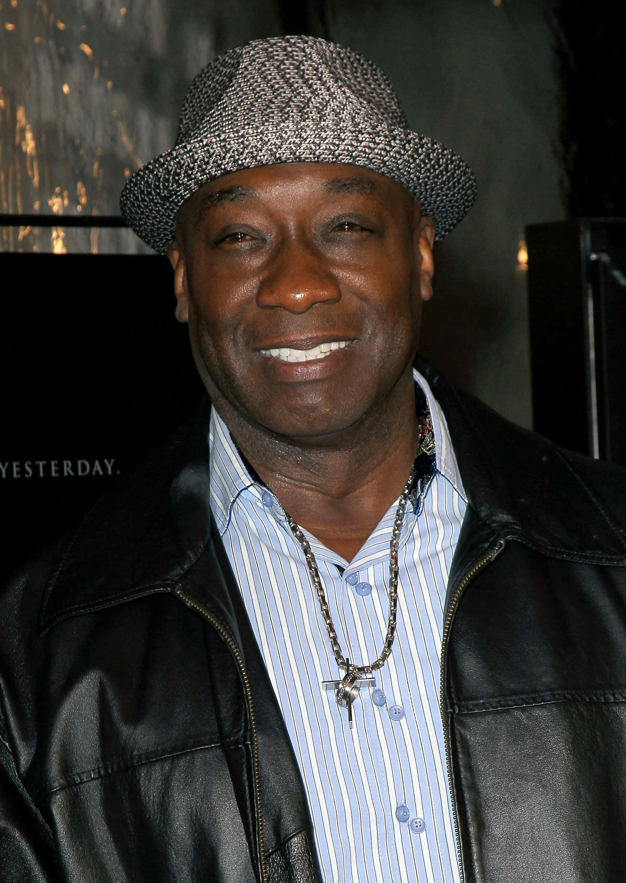 Michael Clarke Duncan 桌布 壁紙 — 一位戴著圖案帽子、皮夾克和條紋襯衫的微笑男士在活動中自信地擺姿勢。
