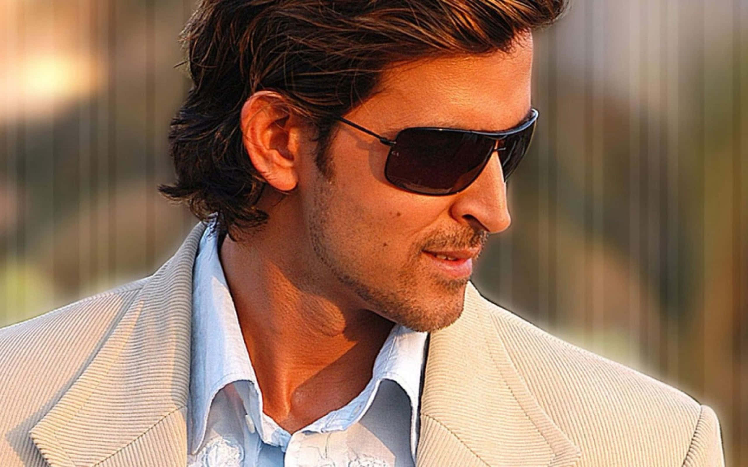 Bollywood Hero 桌布 壁紙 — 一位戴著太陽眼鏡、身穿淺色西裝的時尚男士，在溫暖的金色背景下若有所思地凝視著。