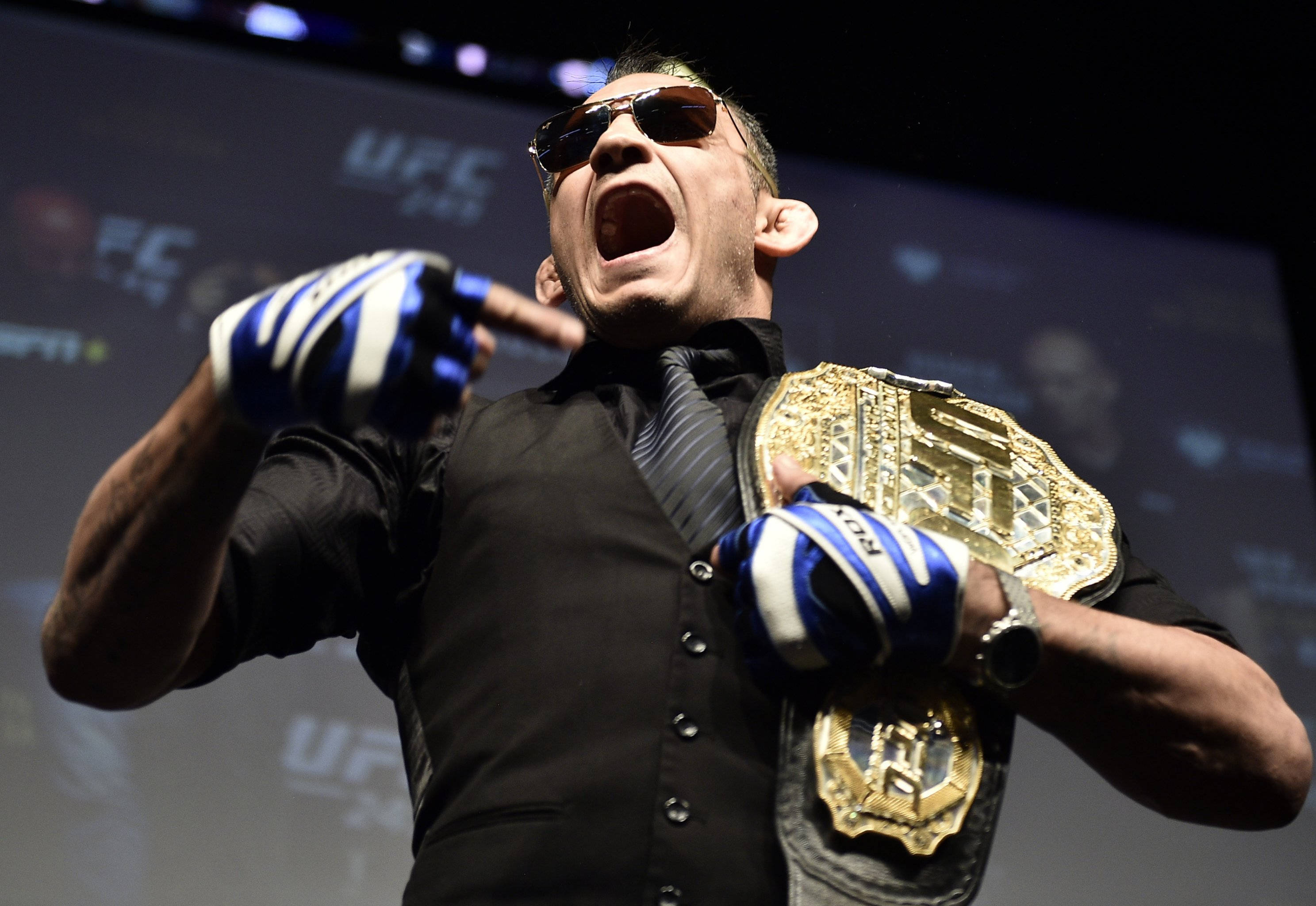 UFC 桌布 壁紙 — 一位戴著太陽眼鏡和手套的UFC拳手在記者會上高舉冠軍腰帶咆哮。