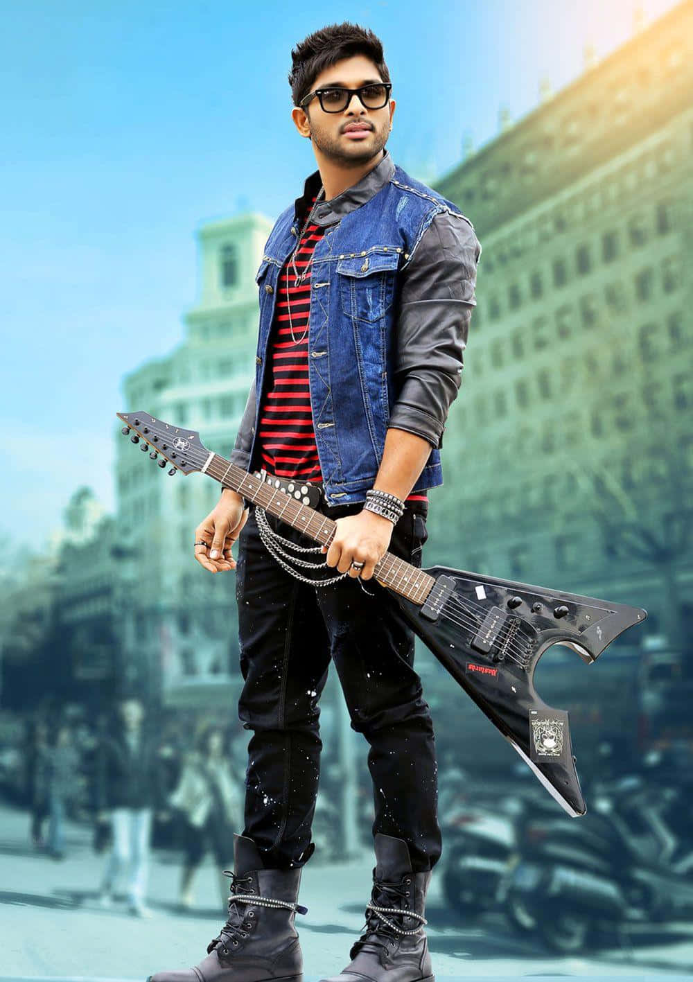 Allu Arjun 桌布 壁紙 — 一位戴著太陽眼鏡和牛仔背心的時尚年輕男子，在模糊的城市背景下自信地拿著一把黑色電吉他。
