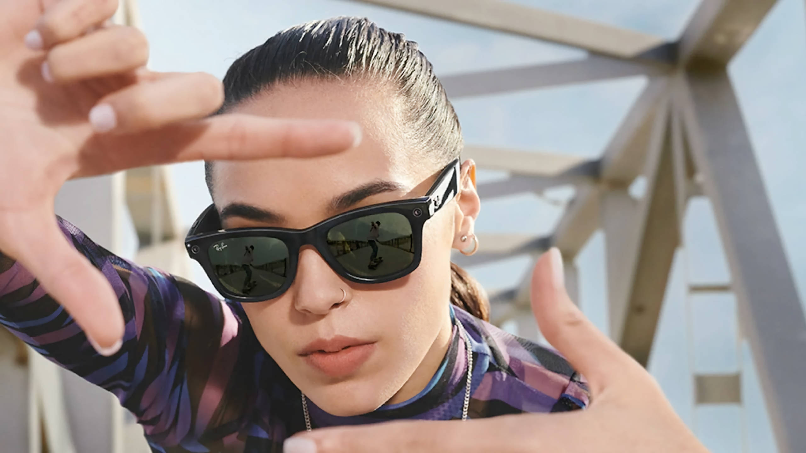 黑色 桌布 壁紙 — 一位戴著太陽眼鏡的女性在明亮的日光下，以雙手框住臉龐，背景是現代金屬結構。