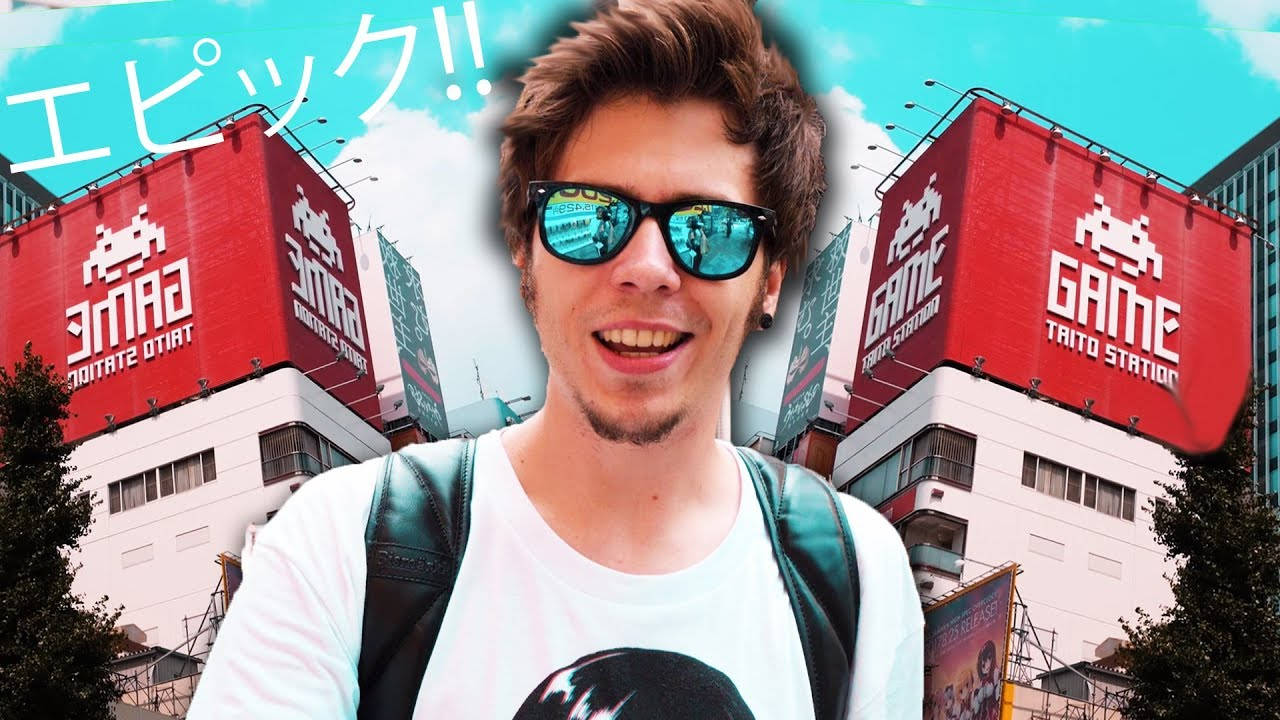 日本 桌布 壁紙 — 一位戴著太陽眼鏡的年輕男子微笑著站在充滿活力的城市環境中，巨大的紅色遊戲廳廣告牌前。