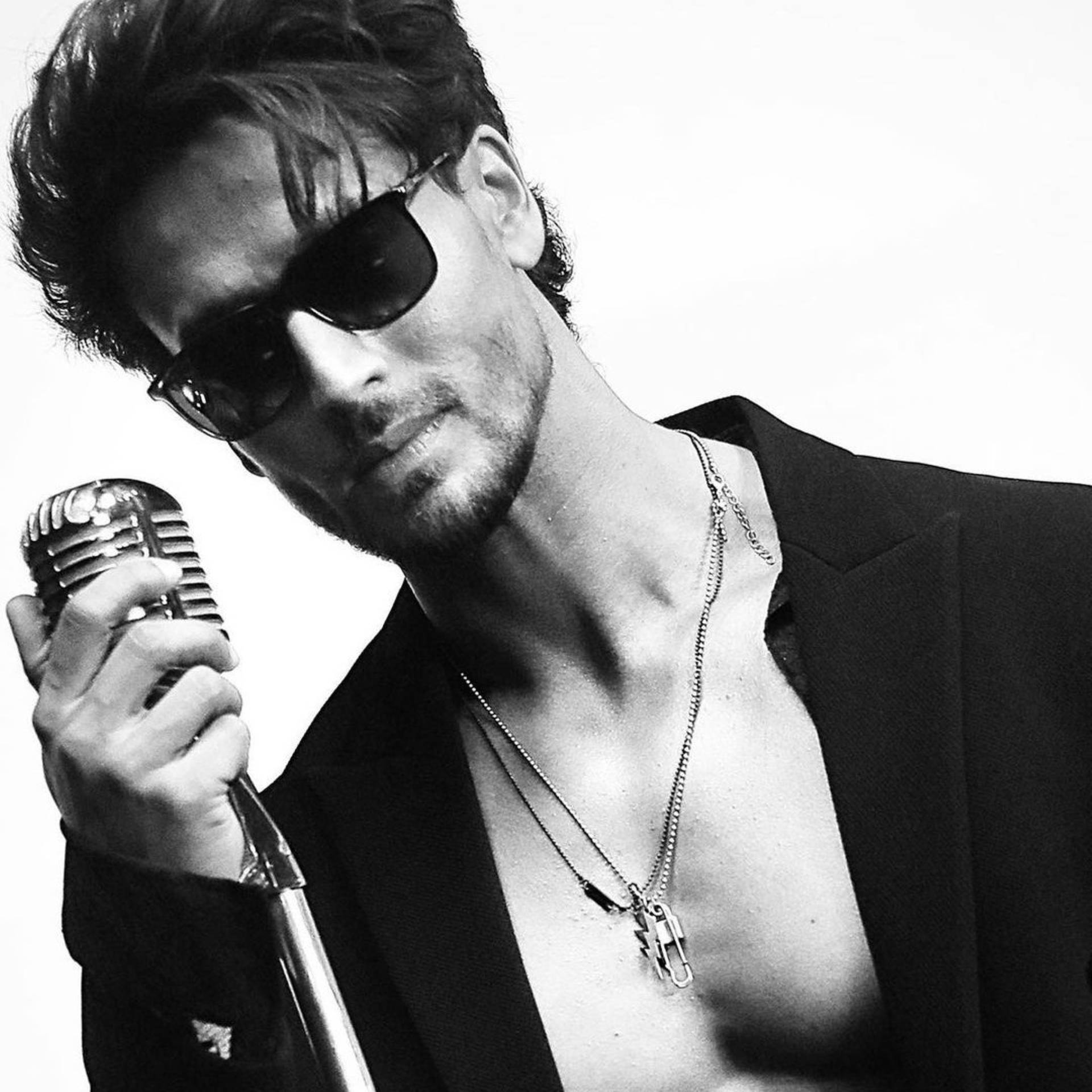 Tiger Shroff 桌布 壁紙 — 一位戴著太陽眼鏡的時尚男士，在單色純白背景前手持復古麥克風。