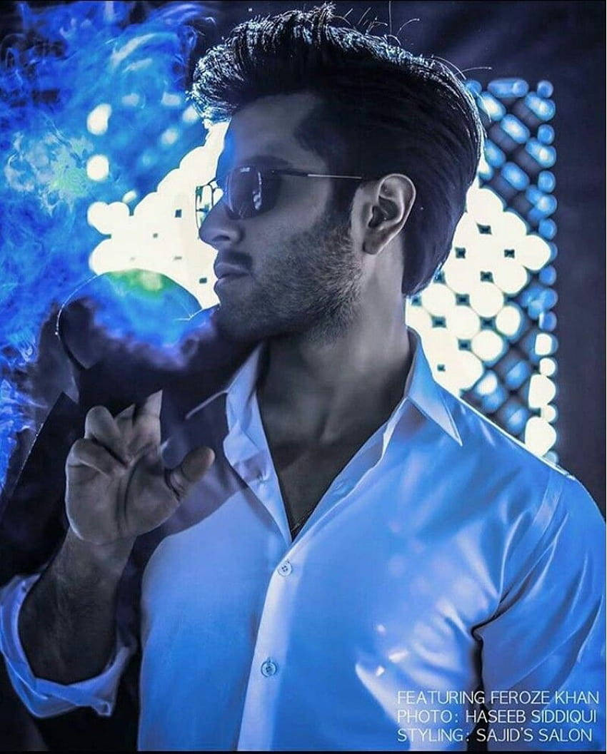 Feroz Khan 桌布 壁紙 — 一位戴著太陽眼鏡的時尚男士，在發光的幾何光背景前呼出鮮豔的藍色煙霧。
