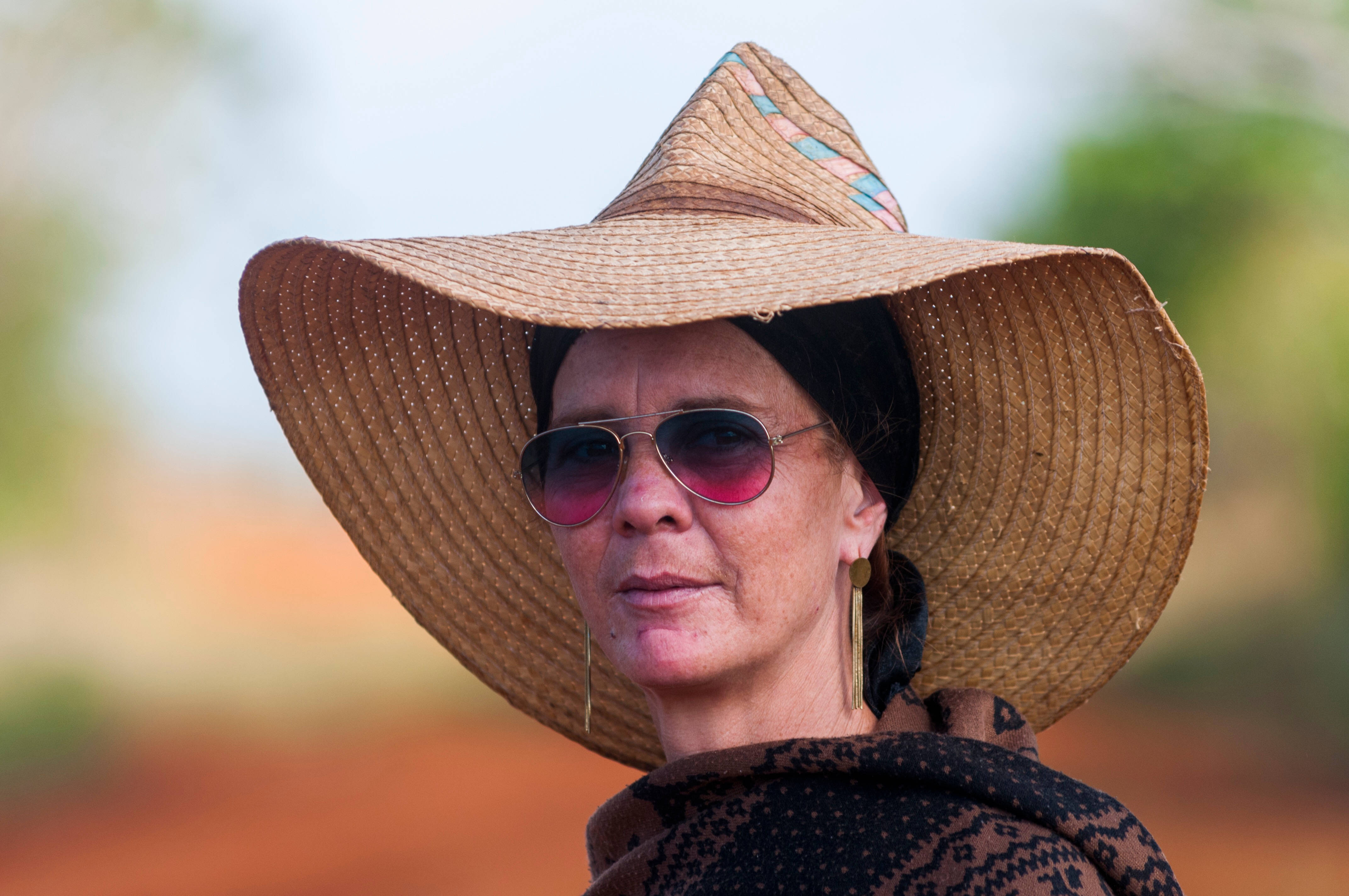 Cuba 桌布 壁紙 — 一位戴著寬邊草帽和紅色太陽眼鏡的女性，在柔和模糊的大地色背景下平靜地凝視著鏡頭。