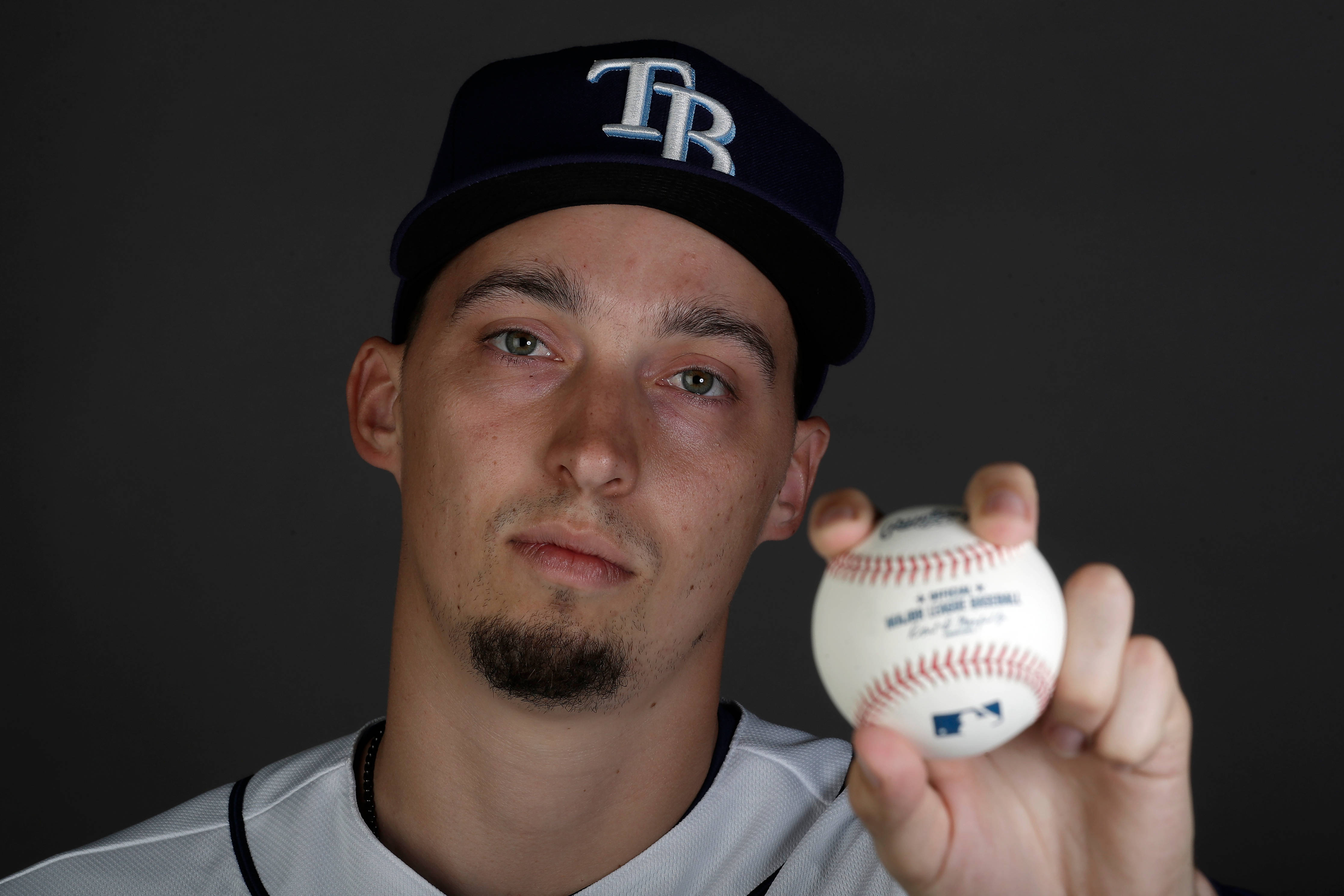 Blake Snell 桌布 壁紙 — 一位戴著帽子的年輕棒球運動員，在昏暗的攝影棚背景下，手持棒球，光線聚焦。