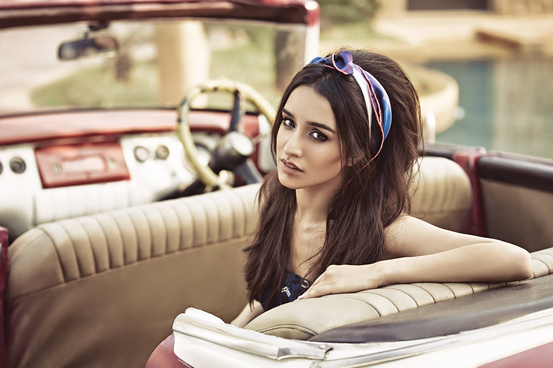 Shraddha Kapoor 桌布 壁紙 — 一位戴著彩色頭帶的年輕女子從一輛米色皮革座椅的復古紅色敞篷車中探出身子。