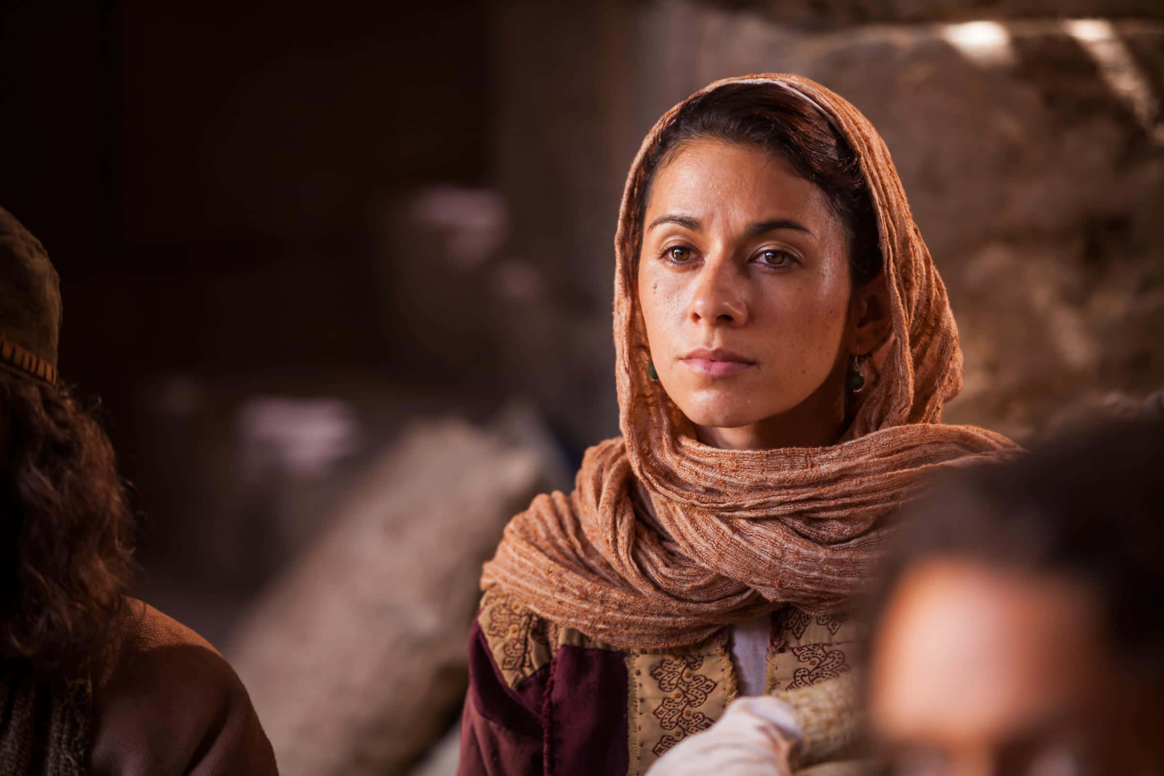 Mary Magdalene 桌布 壁紙 — 一位戴著暖色調頭巾的女性在昏暗的鄉村石頭環境中專注地凝視。