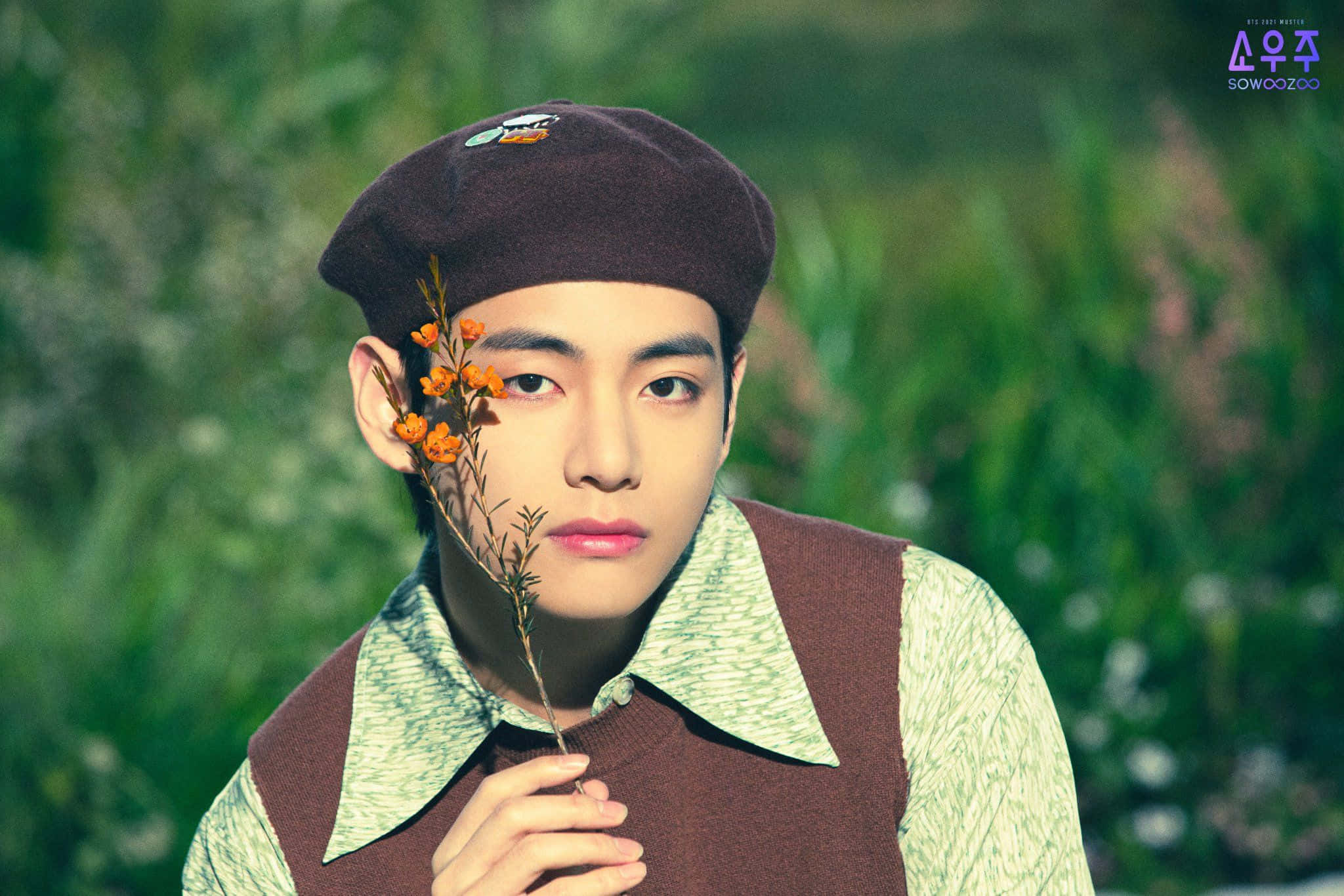 Taehyung Cute 桌布 壁紙 — 一位戴著棕色貝雷帽的年輕男子，手持一枝橙色花朵靠近臉龐，背景是柔和模糊的綠色。