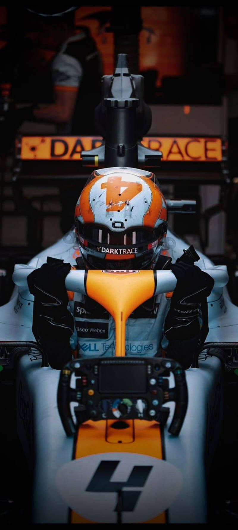Racing 桌布 壁紙 — 一位戴著橙色和白色頭盔的F1車手，在戲劇性的車庫燈光下，抓緊帶有4號的賽車方向盤。