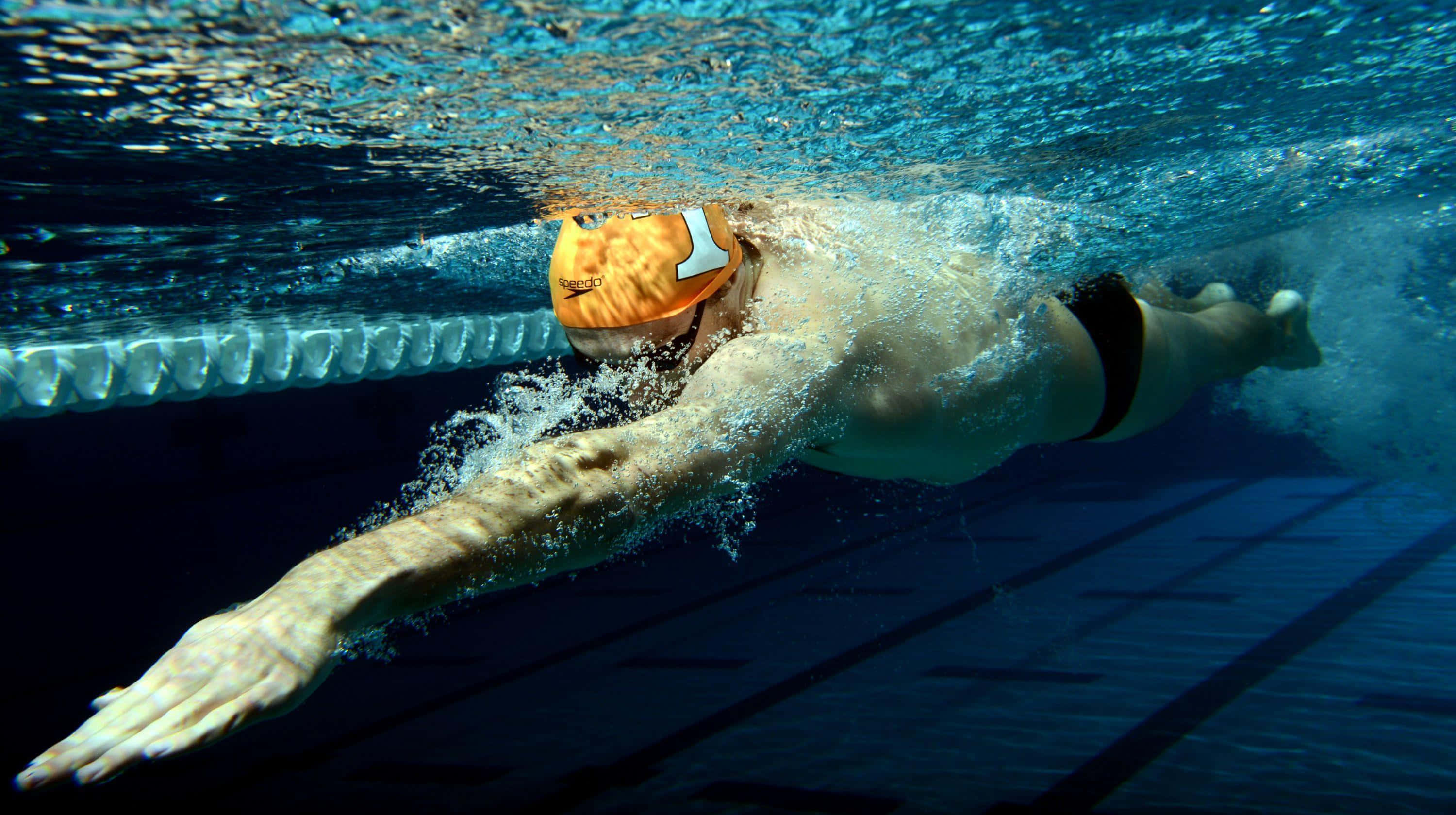 Swimming 桌布 壁紙 — 一位戴著橙色泳帽的泳者在水底沿著泳道滑行，身後留下氣泡。