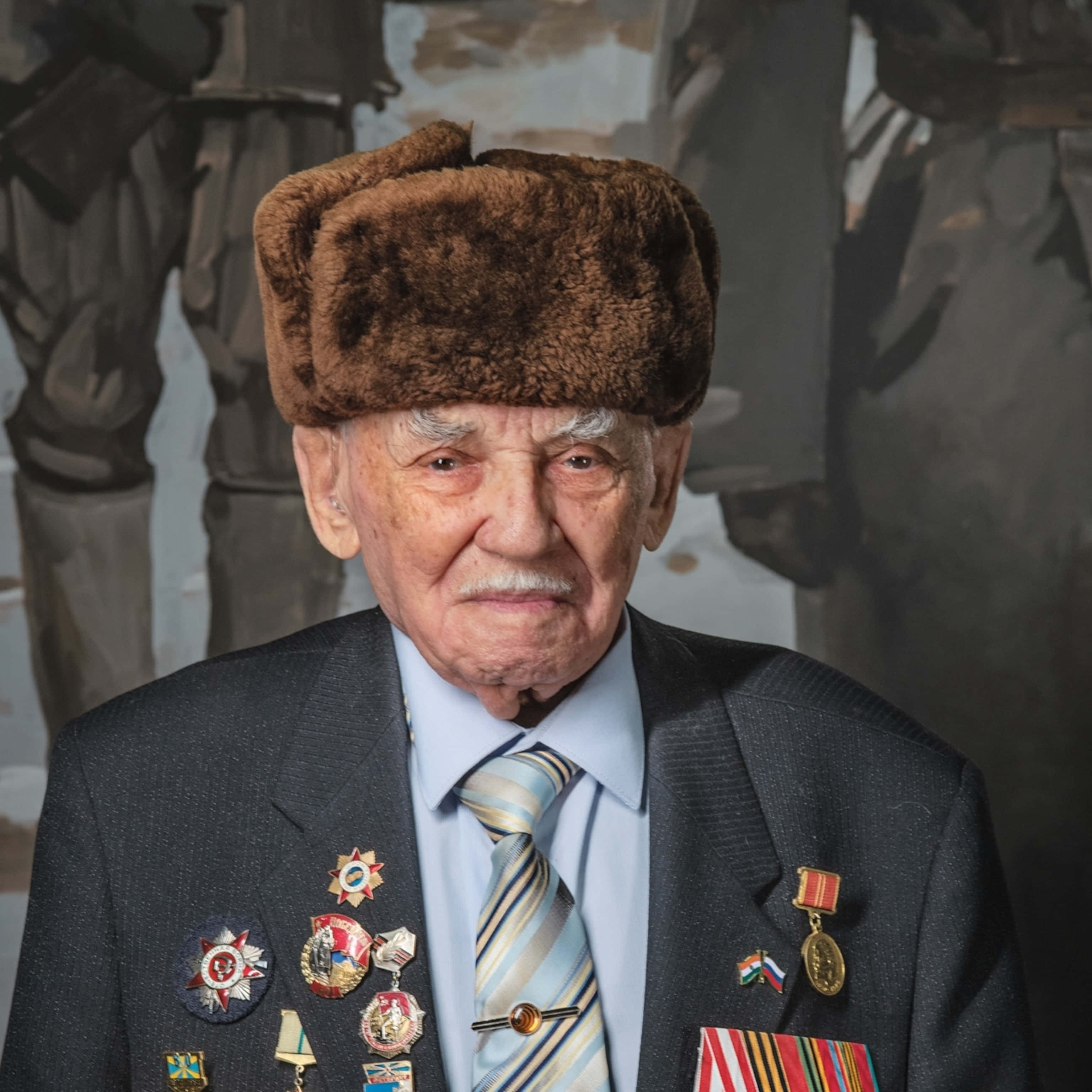 Ww2 桌布 壁紙 — 一位戴著毛帽、穿著裝飾西裝的年長退伍軍人，在柔和的軍事壁畫背景下莊嚴地凝視。