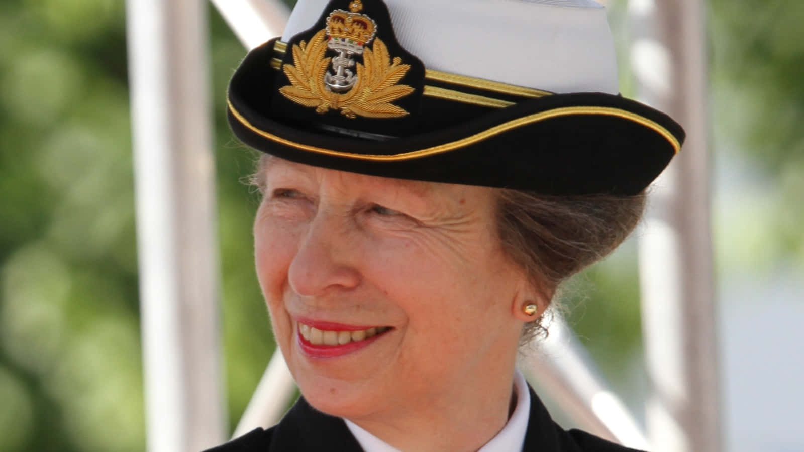 Navy 桌布 壁紙 — 一位戴著海軍軍官帽的老年女性，在模糊的綠色和白色背景前溫暖地微笑。