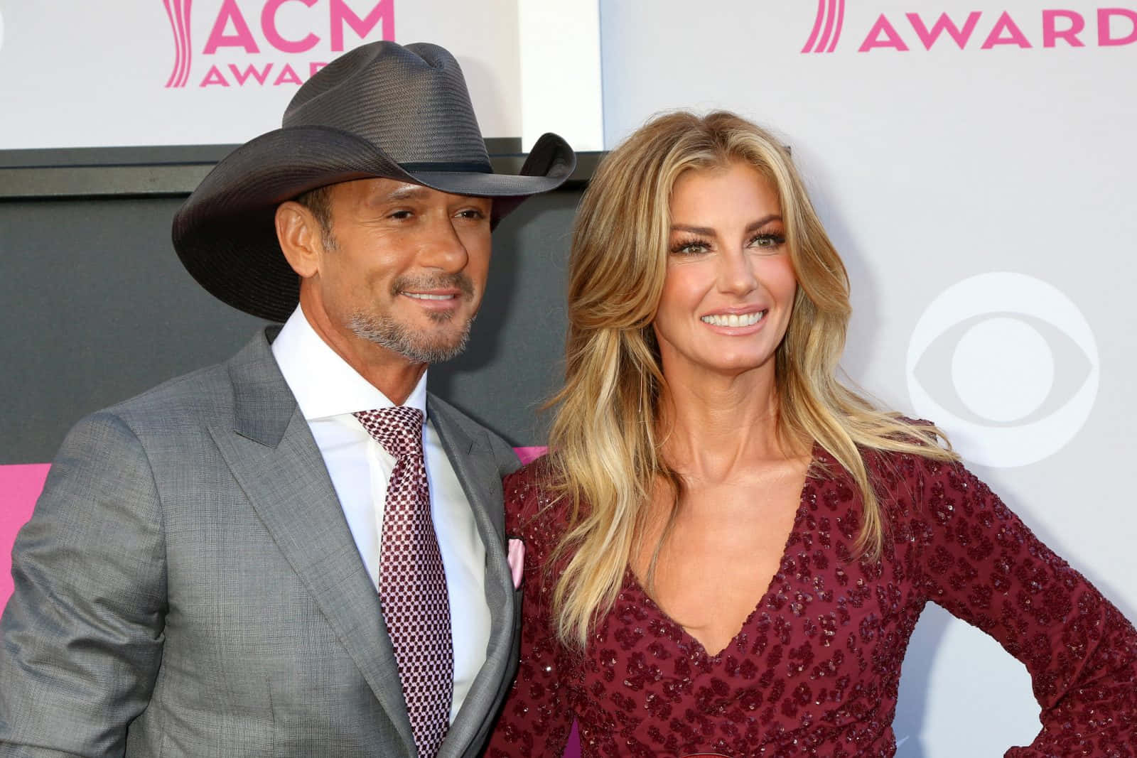 Faith Hill 桌布 壁紙 — 一位戴著牛仔帽、身穿西裝的微笑男士，站在一位身穿閃亮栗色禮服的女士旁邊，在ACM頒獎典禮的紅地毯上。