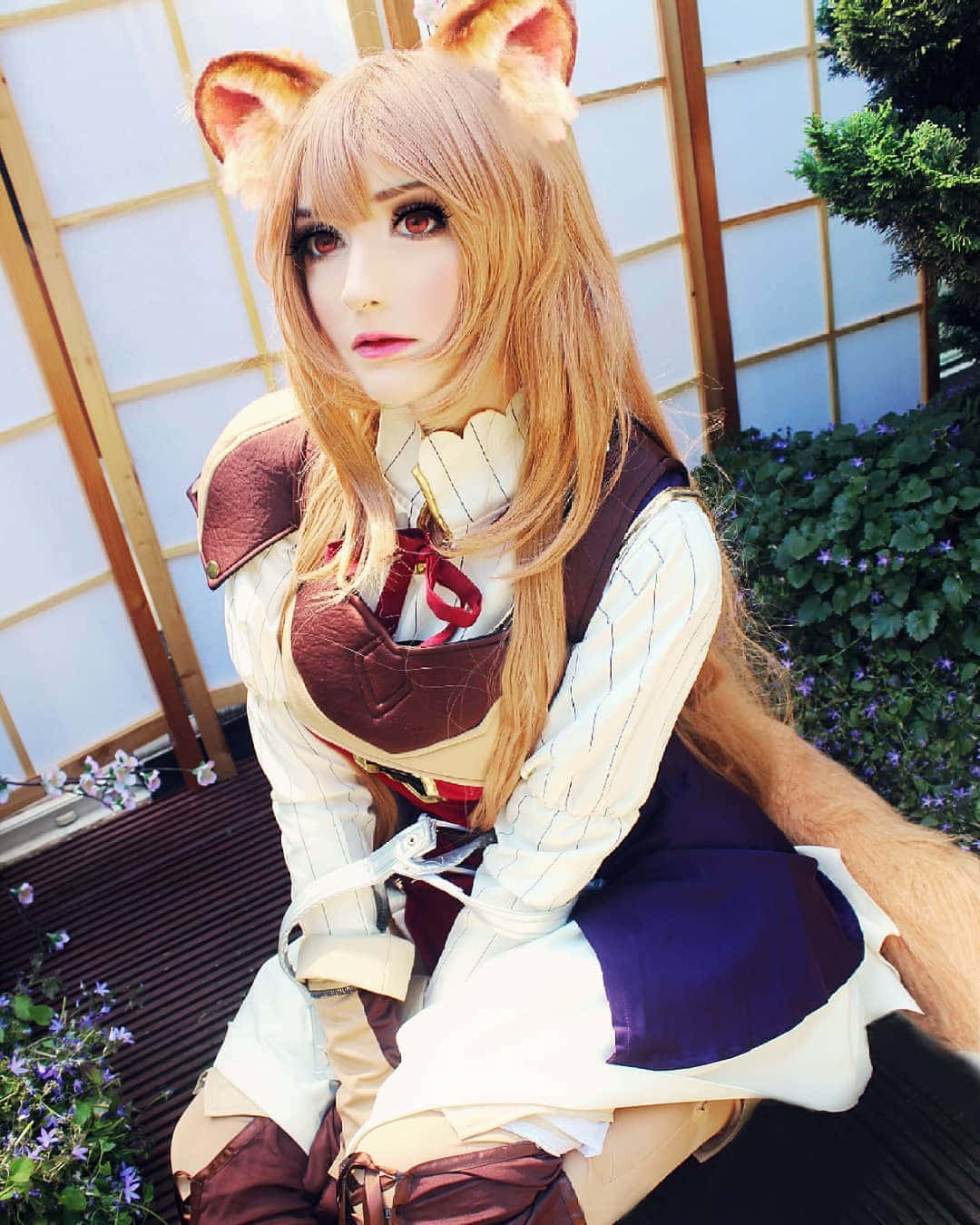 Cosplay Anime Kawaii 桌布 壁紙 — 一位戴著狐狸耳朵和尾巴的cosplayer，穿著精緻的動漫風格服裝，在傳統日本圍欄和開花灌木叢附近戶外擺姿勢。