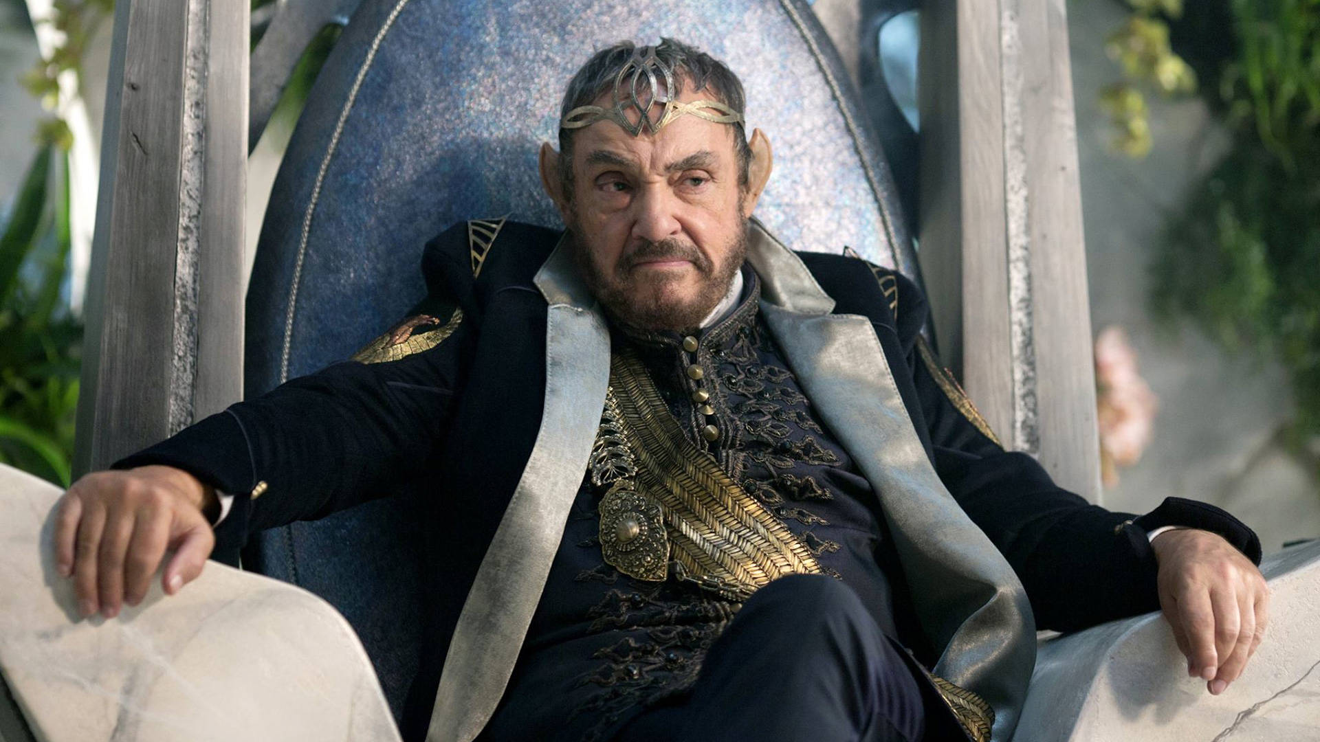 actor 桌布 壁紙 — 一位戴著王冠的威嚴男子坐在華麗的寶座上，身穿黑色和金色刺繡的長袍，配有銀色肩帶。