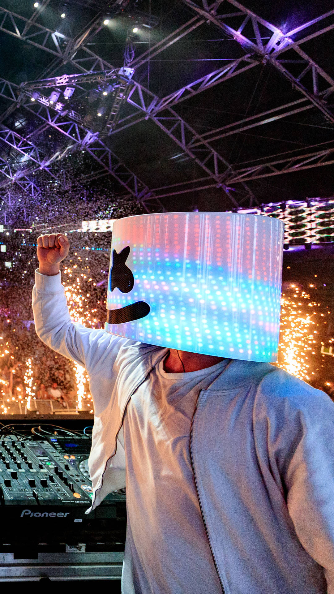 marshmello iPhone 桌布 壁紙 — 一位戴著發光LED棉花糖頭盔的DJ在鋼桁架結構下充滿活力的夜間音樂會上舉起拳頭。