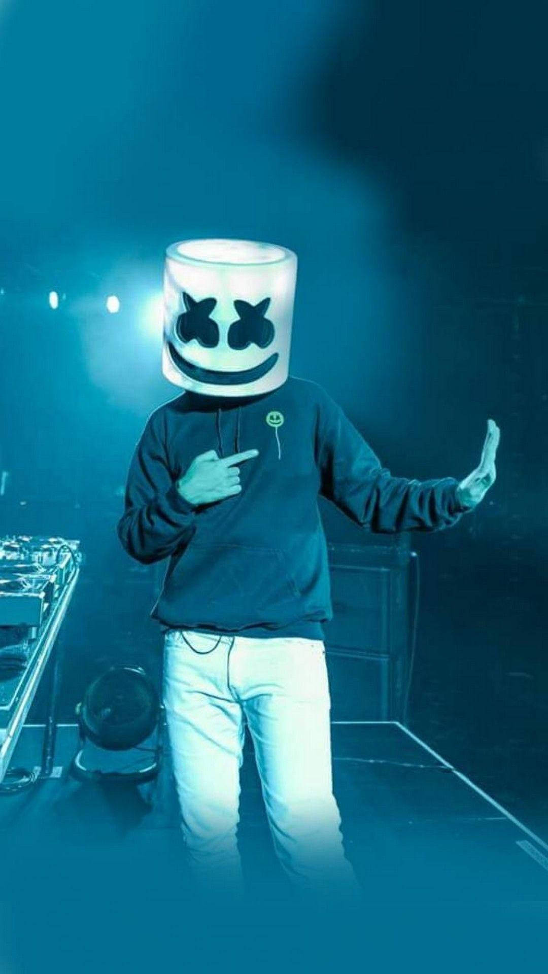 Marshmello 動態圖 桌布 壁紙 — 一位戴著發光白色棉花糖頭盔的DJ在藍色舞台燈光下指向相機。