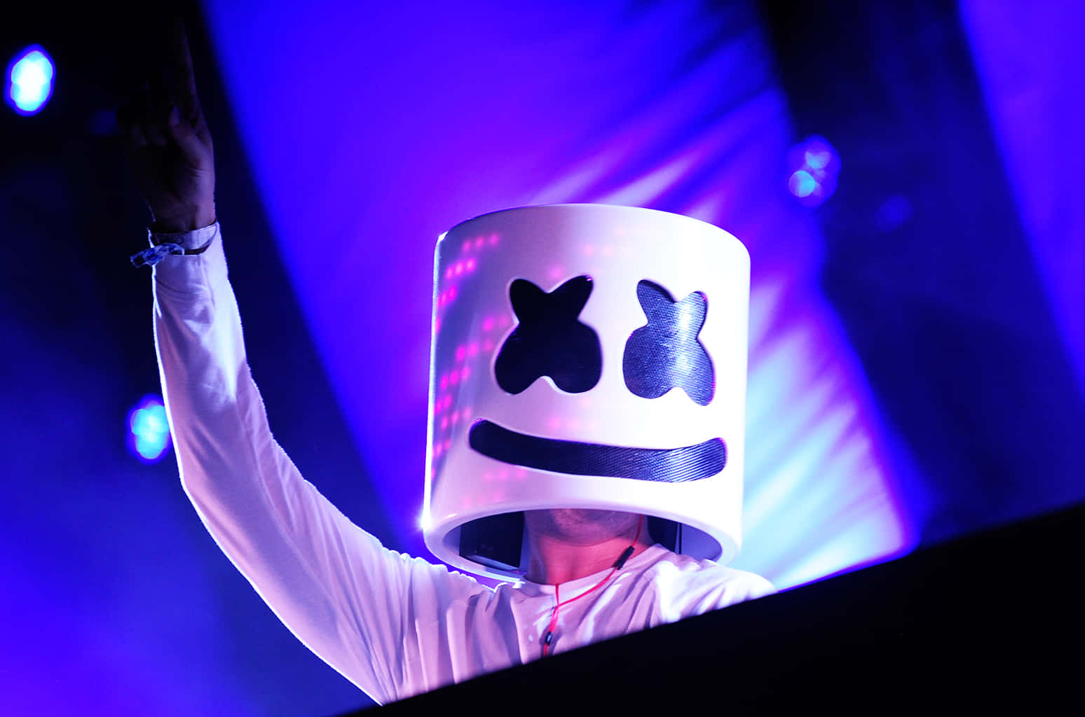 Marshmello 動態圖 桌布 壁紙 — 一位戴著發光白色棉花糖頭盔的DJ在充滿活力的紫色舞台燈光下舉起一隻手臂。