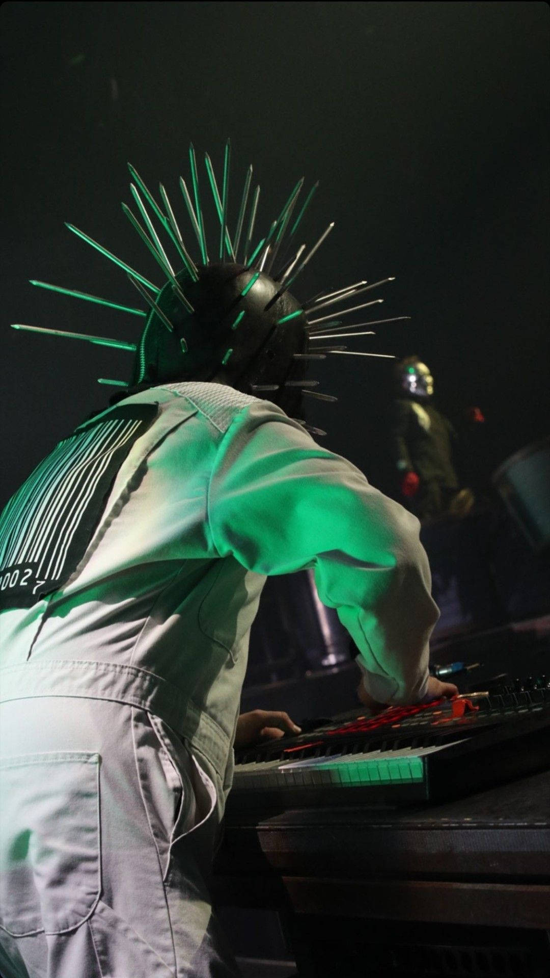 craig jones 桌布 壁紙 — 一位戴著發光綠色尖刺頭盔的音樂家在舞台燈光下彈奏鍵盤。